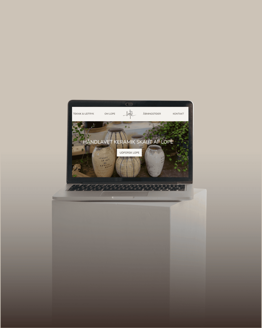 Computer der viser keramik website, omgivet af en beige baggrund