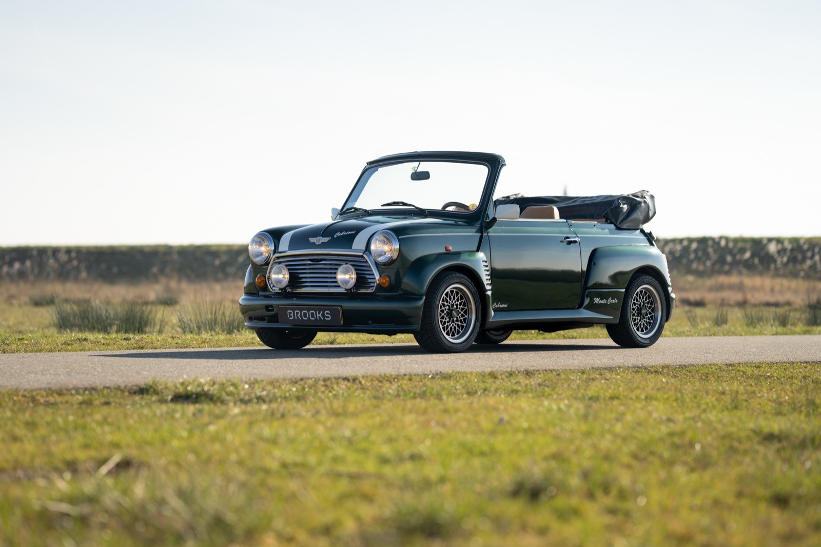 A convertible car parked on a scenic road, surrounded by open green fields under a clear sky.