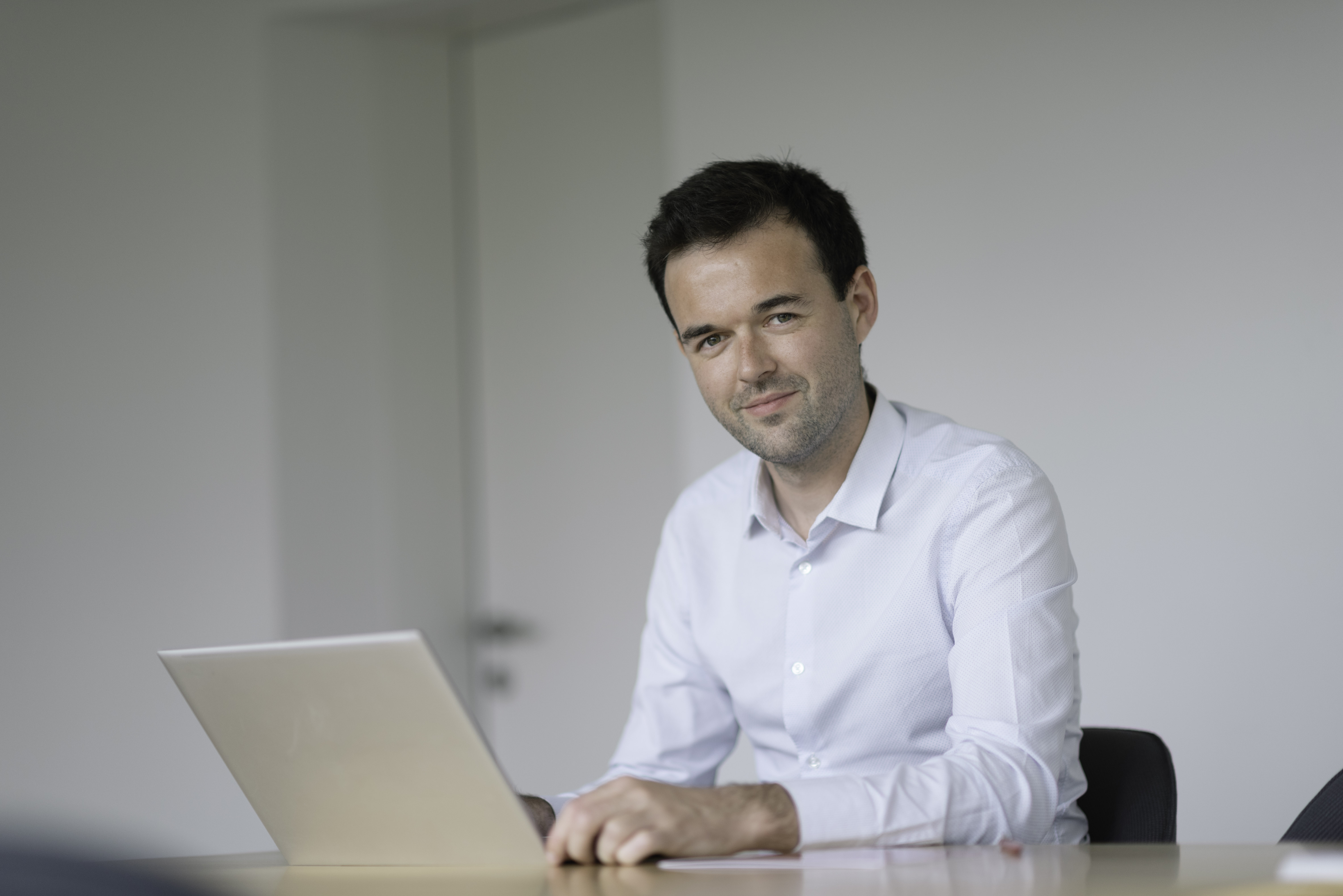 Professional portrait of a Team member, sitting at a table with a laptop and a confident expression.