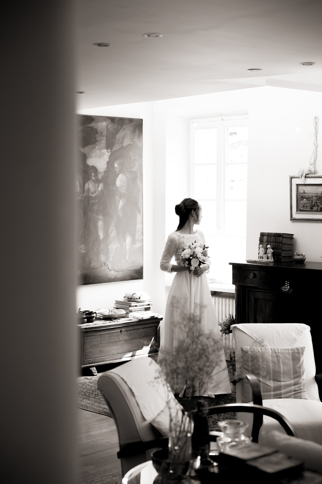 Sposa in abito ricamato di pizzo guarda verso la finestra luminosa durante i preparativi matrimoniali a Villa Peroni Riva