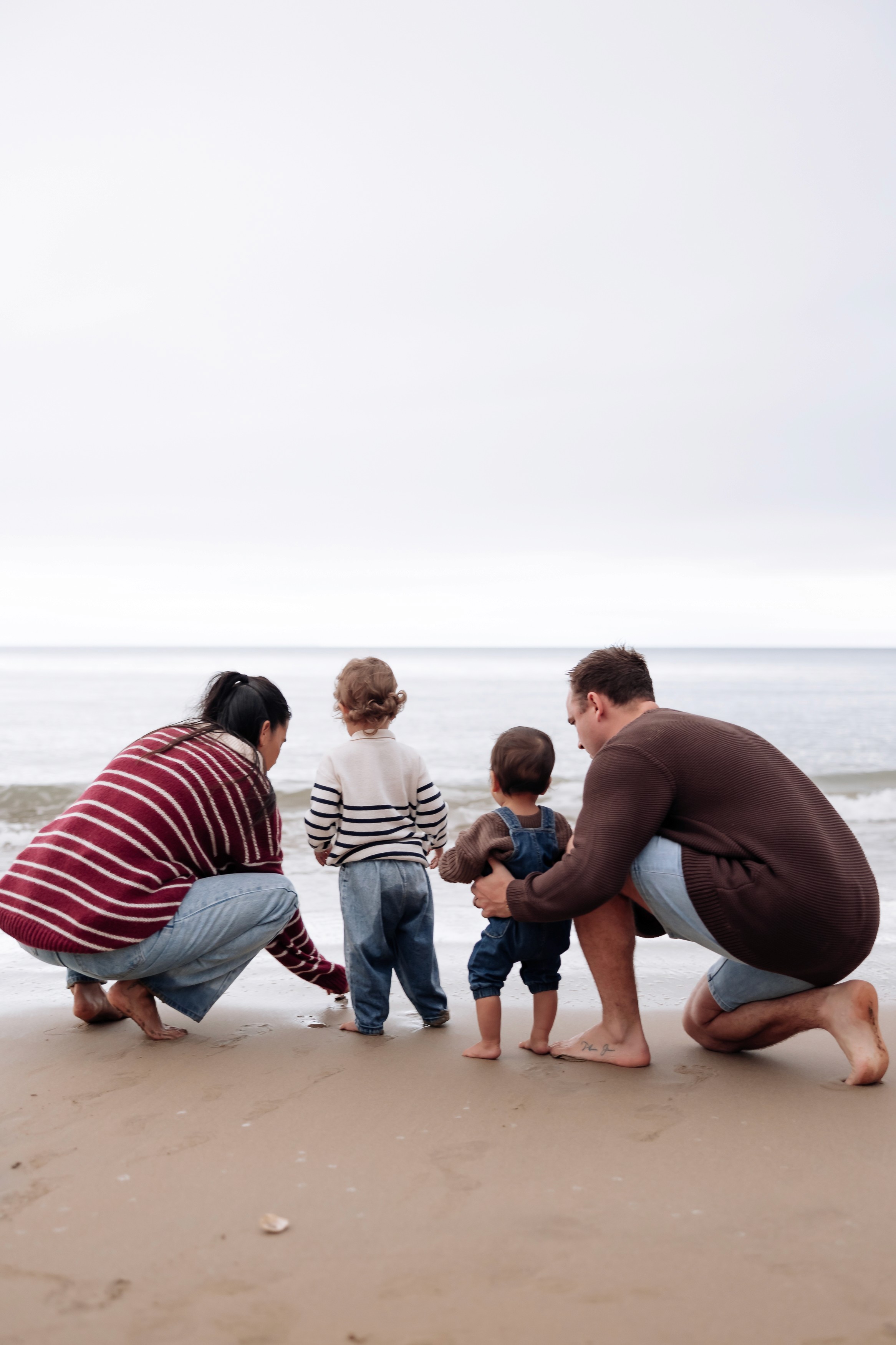 Family embracing barefoot on the beach during a winter sunset session in Mackay, Queensland