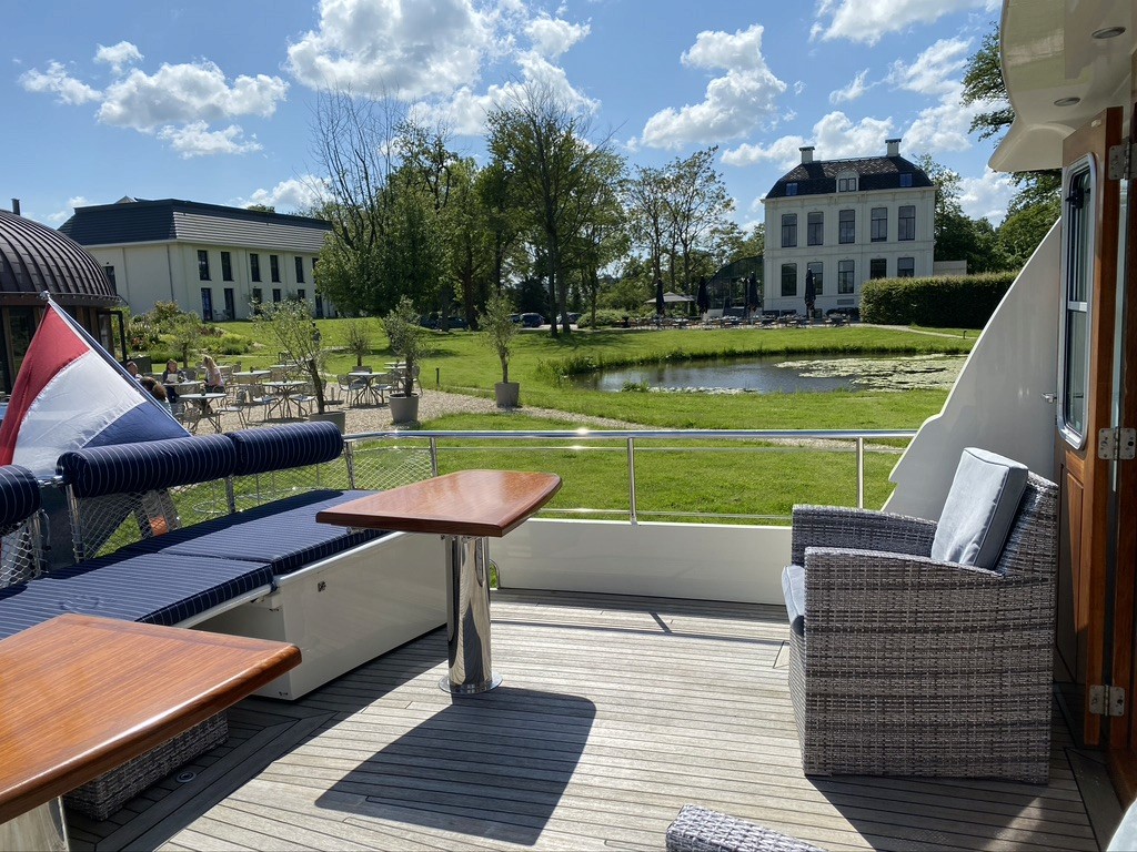 Shaded terrace with arched ceilings and hanging lanterns, beige cushions, earthy pottery, breeze flowing in from the ocean, warm and relaxed mood.