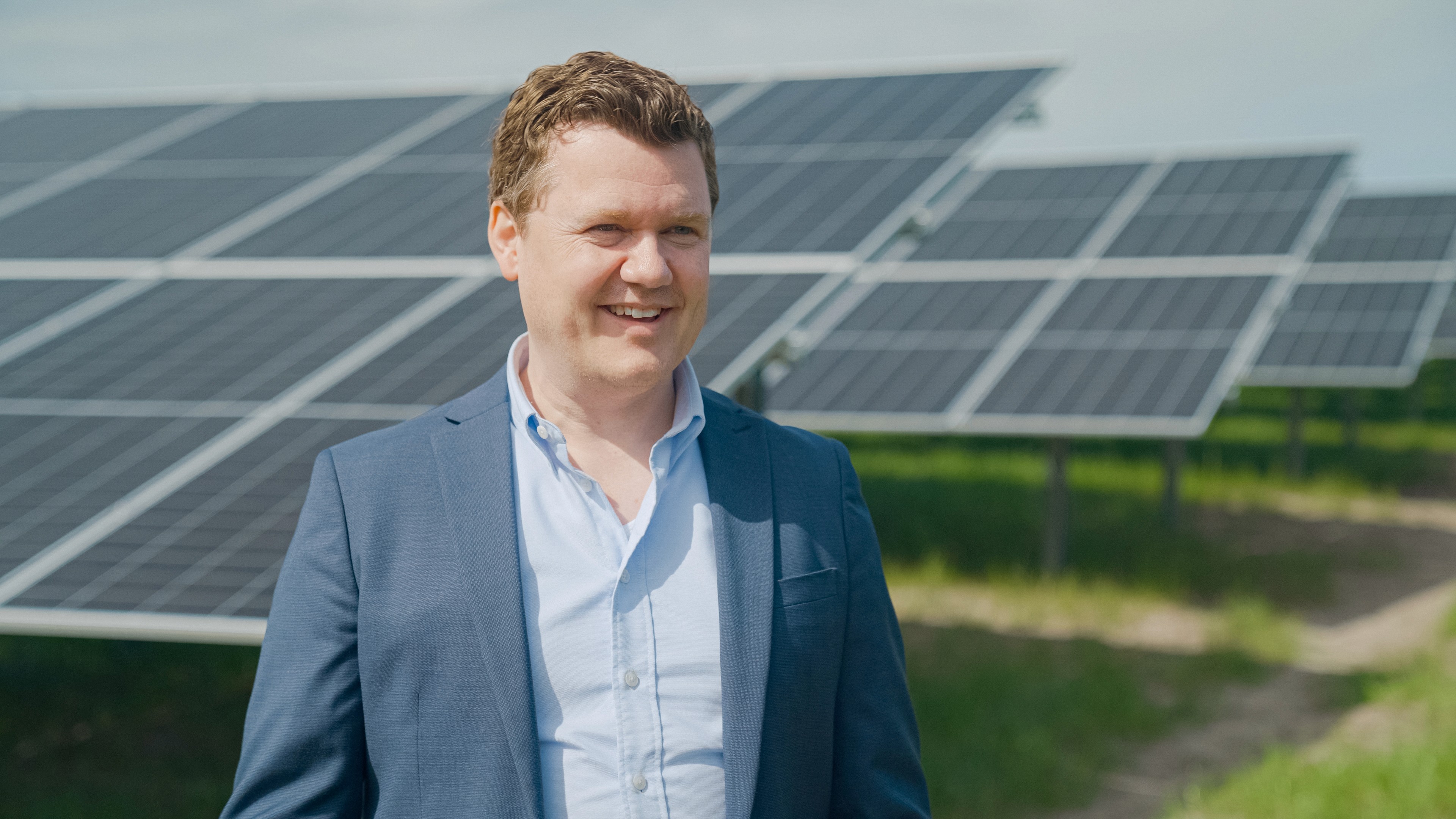 Man standing in a suit and smiling, with solar panels behind him.