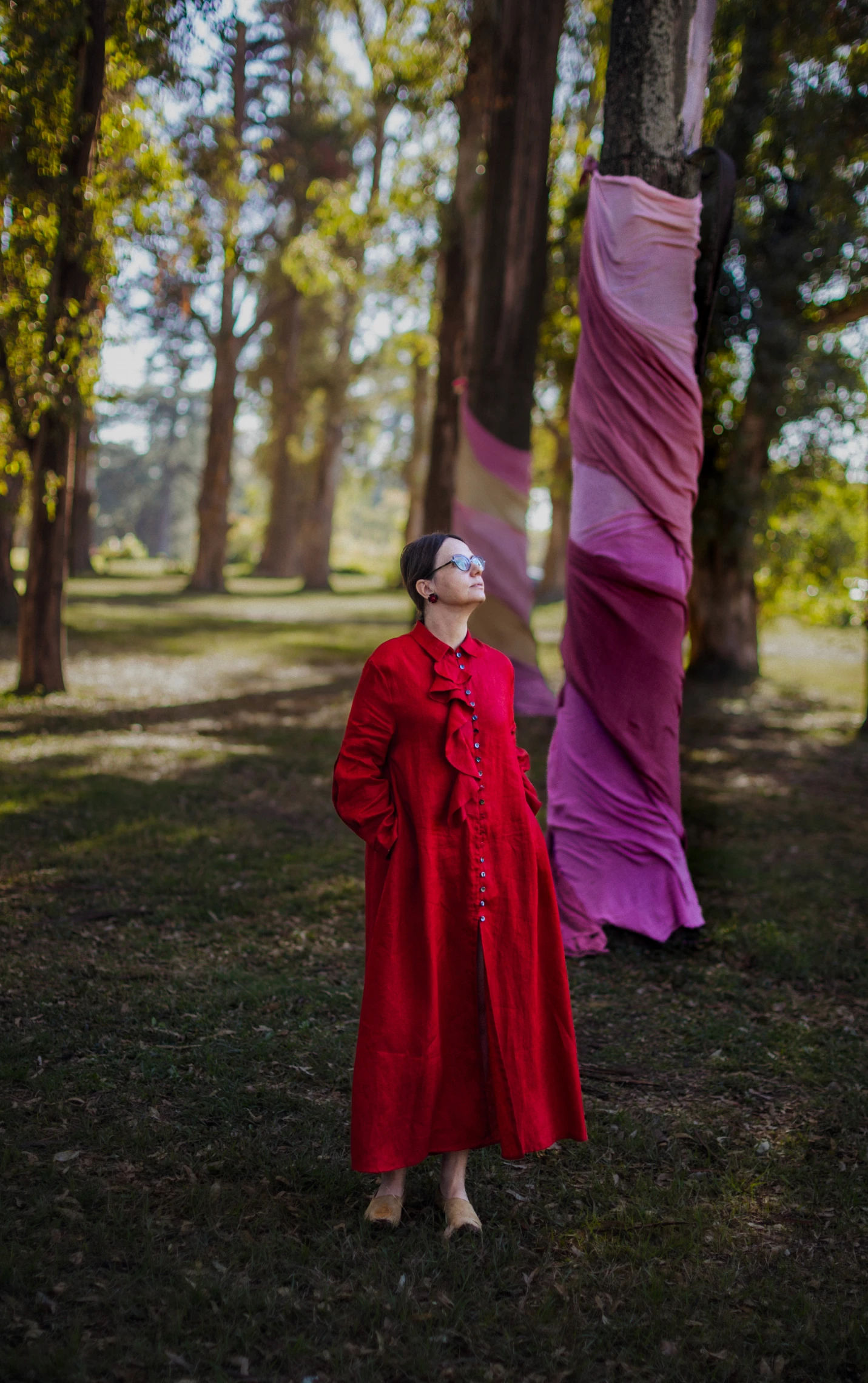 Mujer con vestido rojo junto a árboles envueltos en telas rosas.