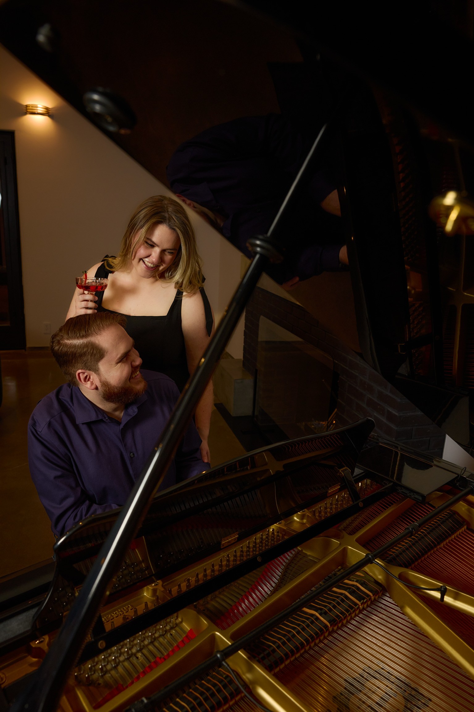 Alex sitting at a grand piano with his wife Tess smiling over his shoulder