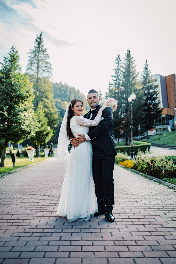 A couple stands hand-in-hand in front of a rustic stone building.