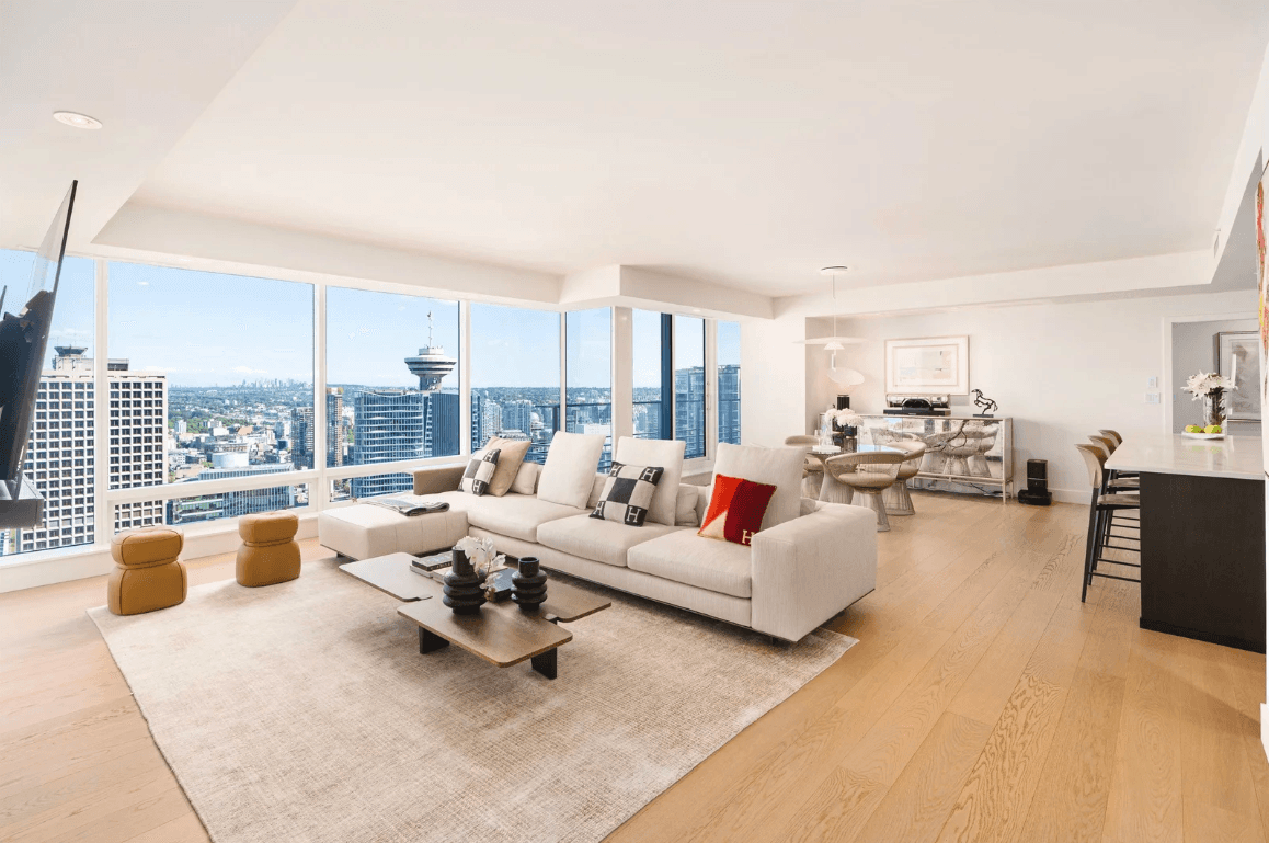 Bright, modern living room with large windows showcasing a city view, featuring a white sofa and stylish decor.