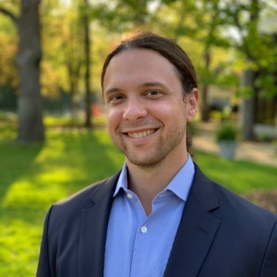 A portrait photo of Ben Flotken, a light-skinned man with short hair wearing a light blue dress shirt with a navy suit jacket.