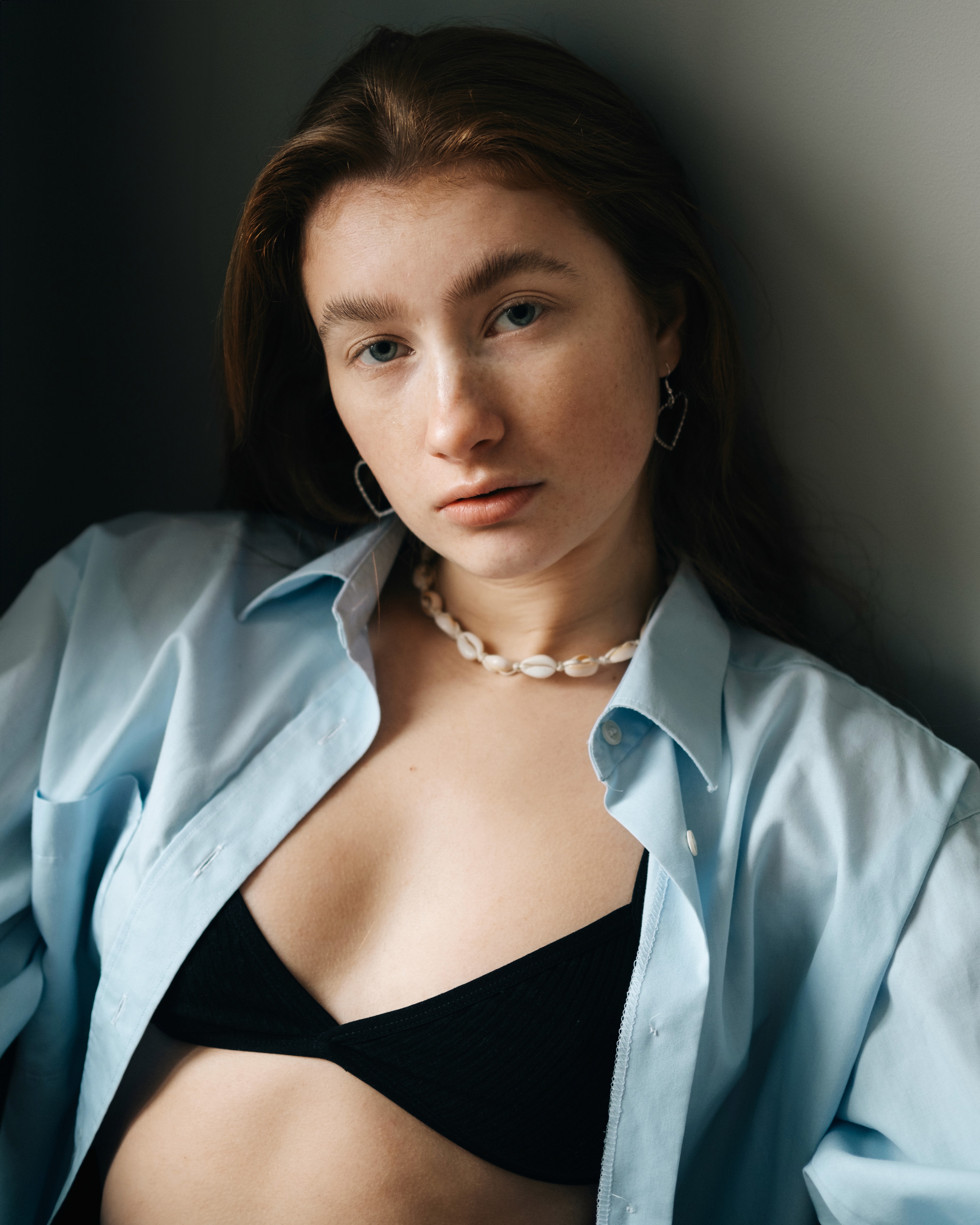 Soft portrait of a person wearing a light blue shirt over a black top, looking calmly into the camera.