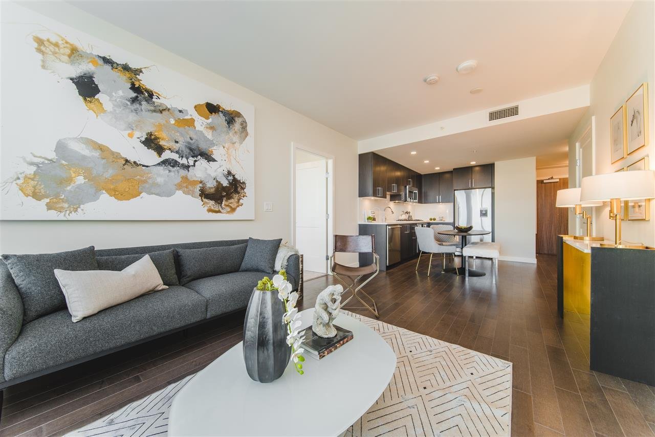 A modern living room featuring a grey sofa, decorative wall art, and an open kitchen in the background.