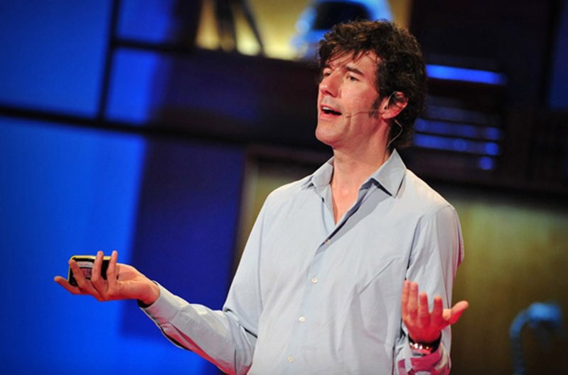 A photo of a person standing on a stage and giving a lecture while holding a remote in his hand.