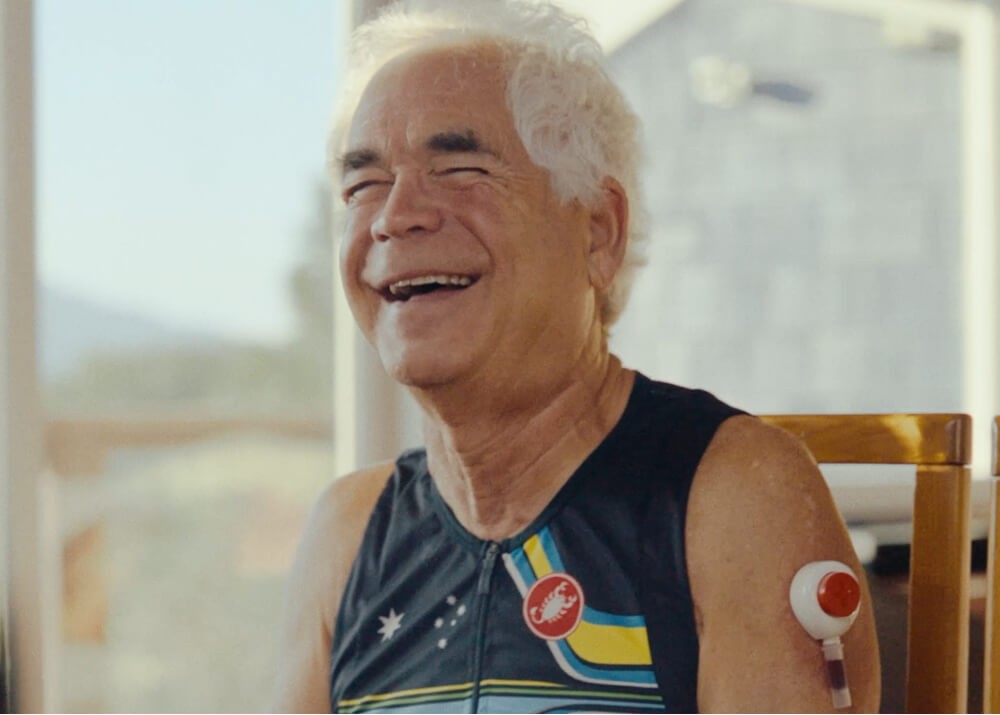 Older man smiling while collecting a blood sample from his upper arm at home.
