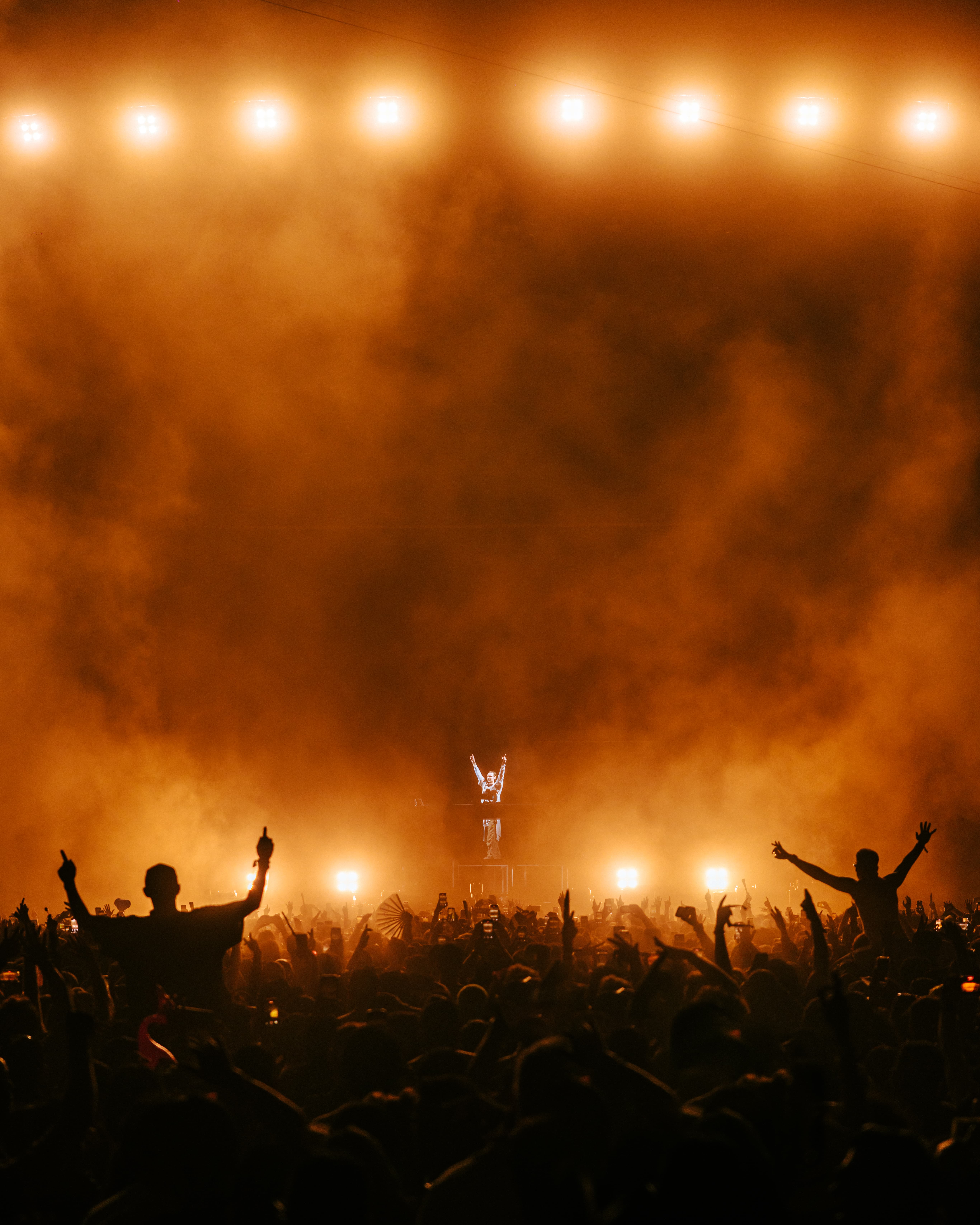 MAU P performing live at Coachella 2025 with arms raised above a packed crowd under warm orange lighting and haze, captured by A World Away creative director Brandon Densley