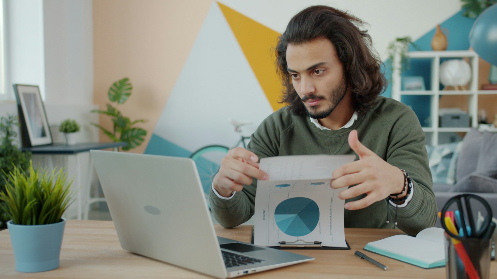 Man looking at laptop and paper in colorful room