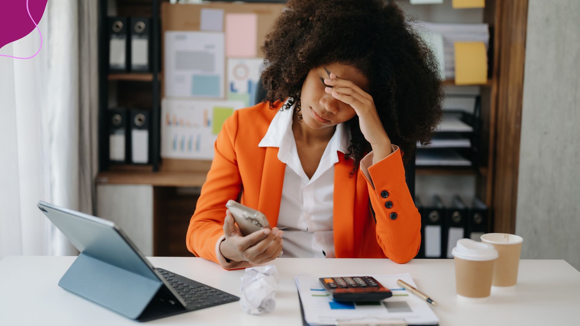 Woman sitting at a desk, stressed looking at phone