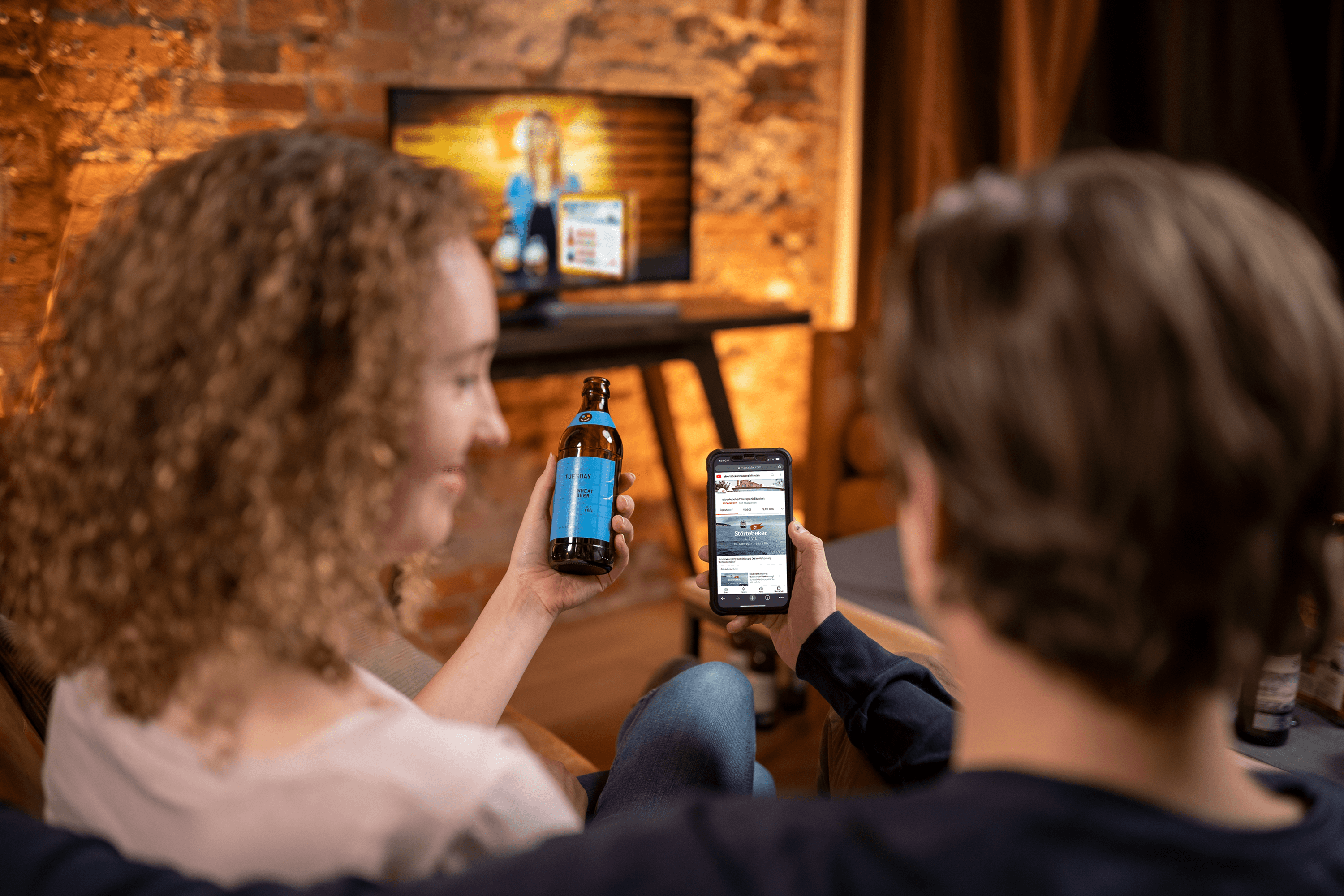 Couple watching TV, one holding beer, other a phone