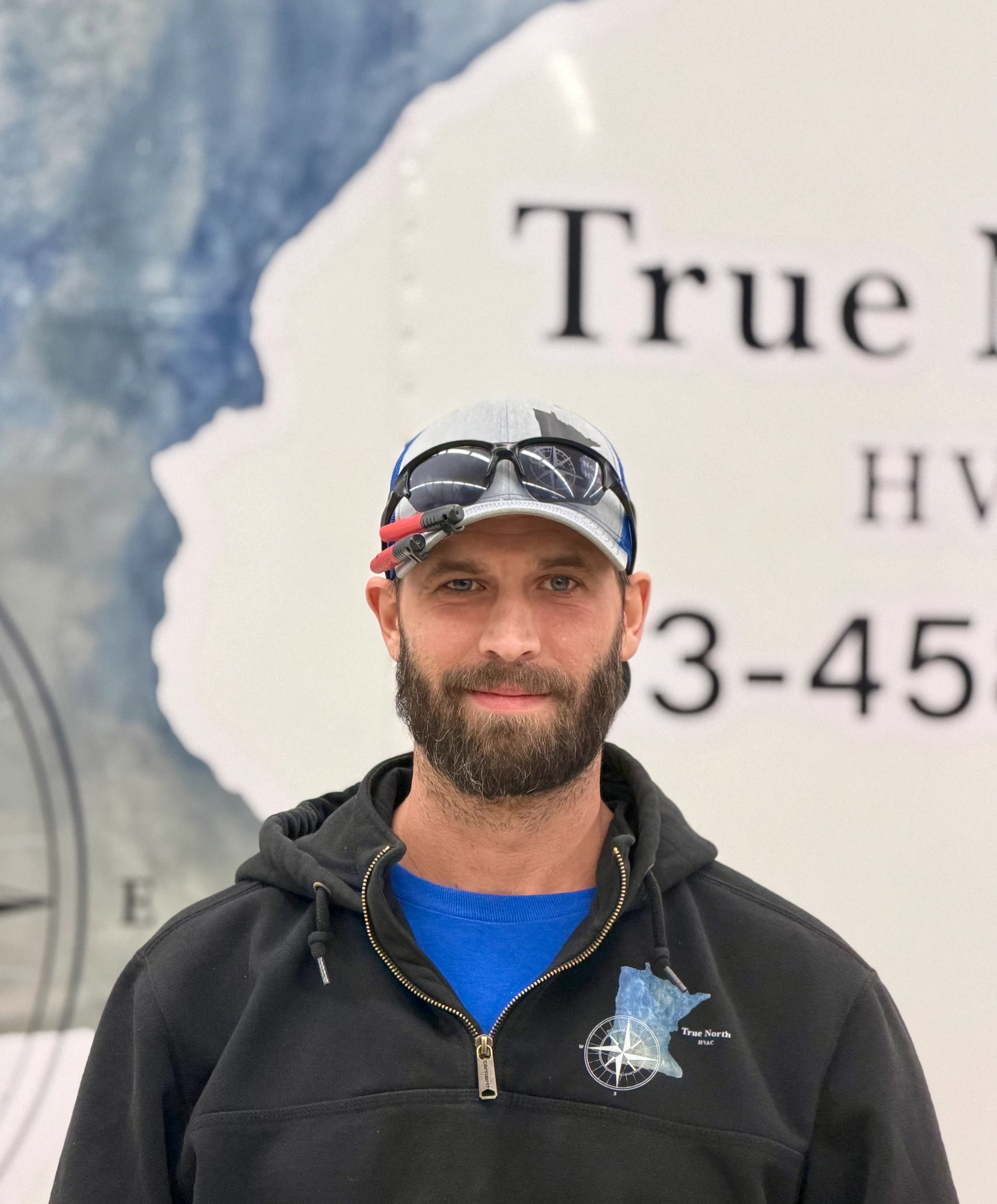 A smiling person with curly hair sits at a desk, looking at a laptop against a dark background.