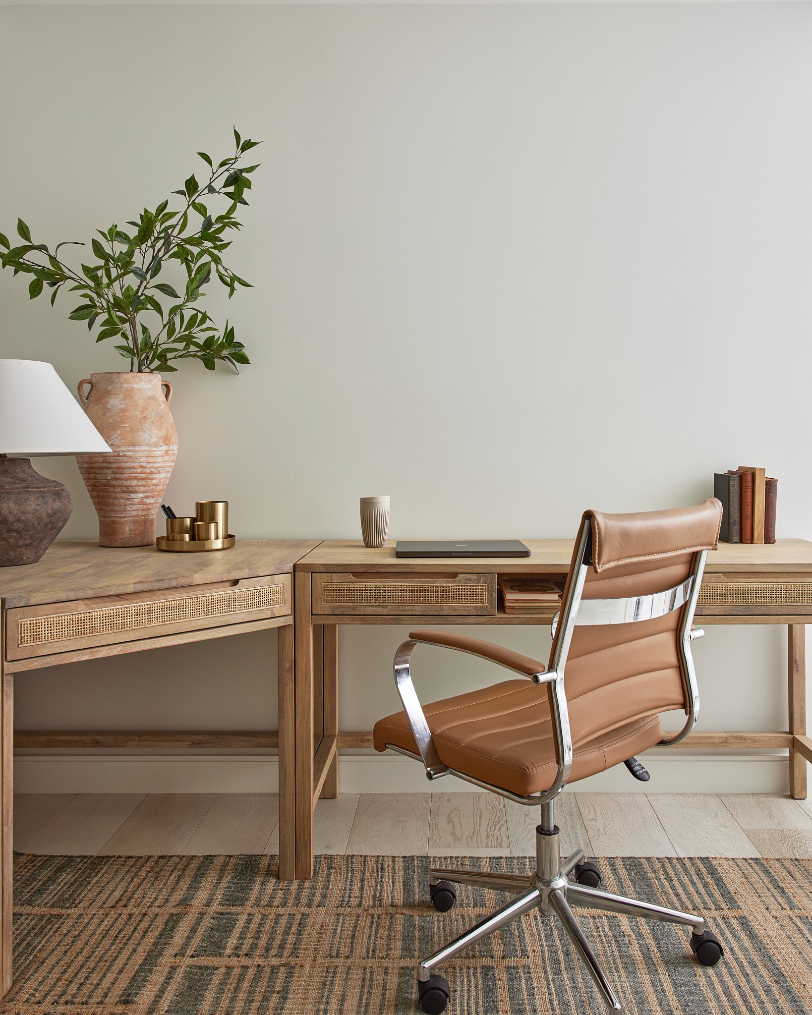 Office with natural tones and textures, modular wood desk, reading table lamp, leather office chair, top down, bottom up blinds, and patterned rug by Jubilee Interiors in Los Angeles, California