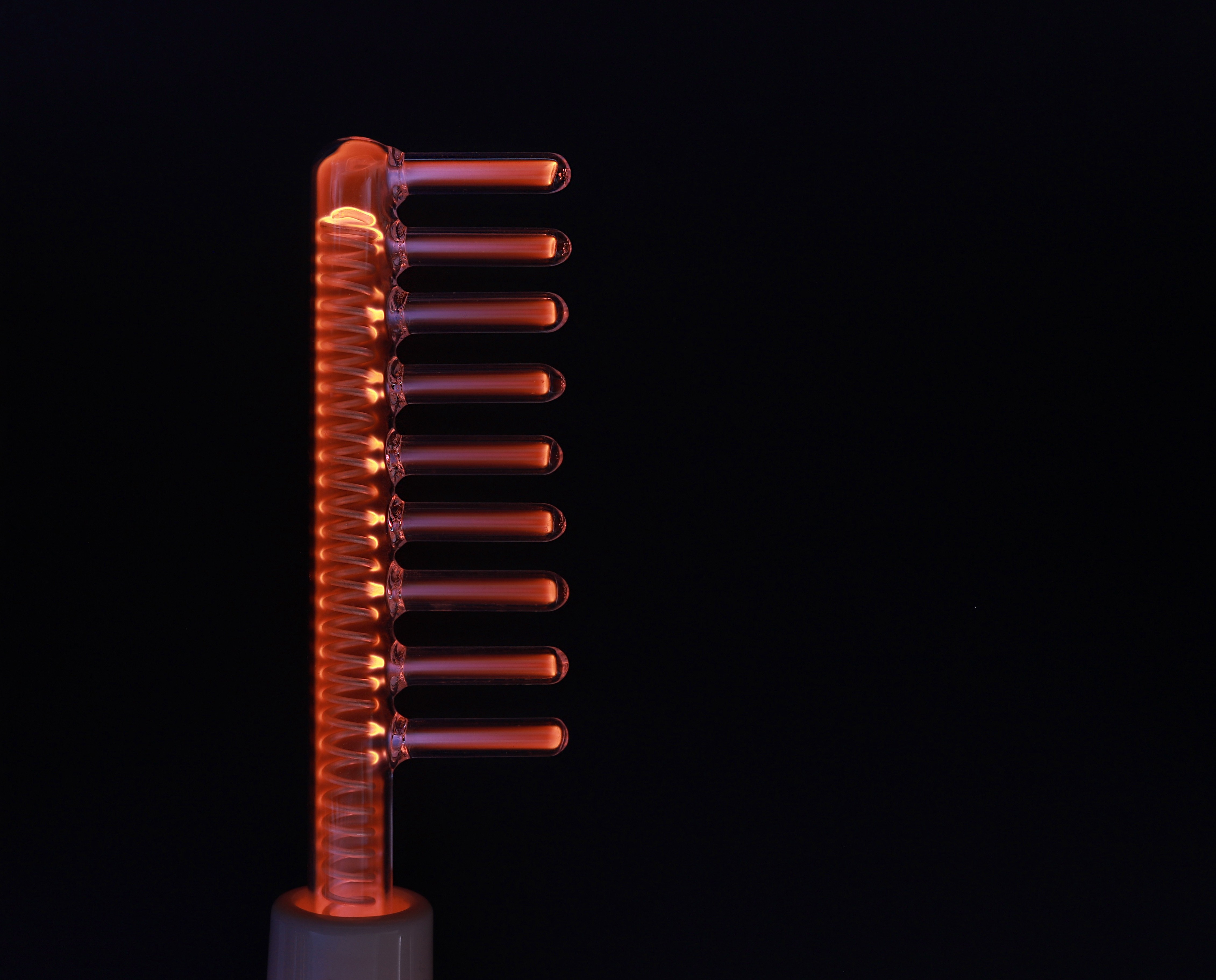 Dispositivo estético de alta frecuencia en Espacio Yutori. Electrodo de vidrio en forma de peine brillando en naranja sobre fondo negro, usado para estimulación capilar o tratamientos faciales.