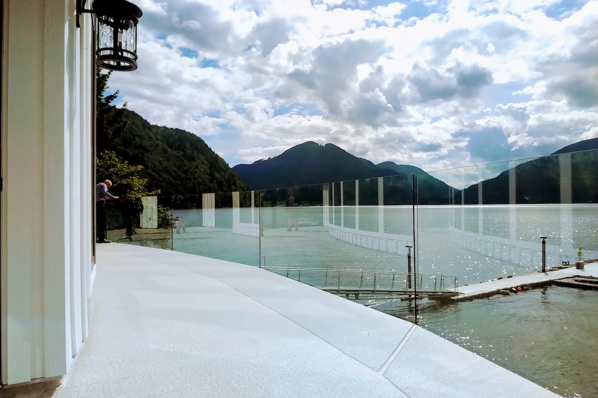 Frameless glass deck railings overlooking the Fraser Valley hills and lake under a bright sky.