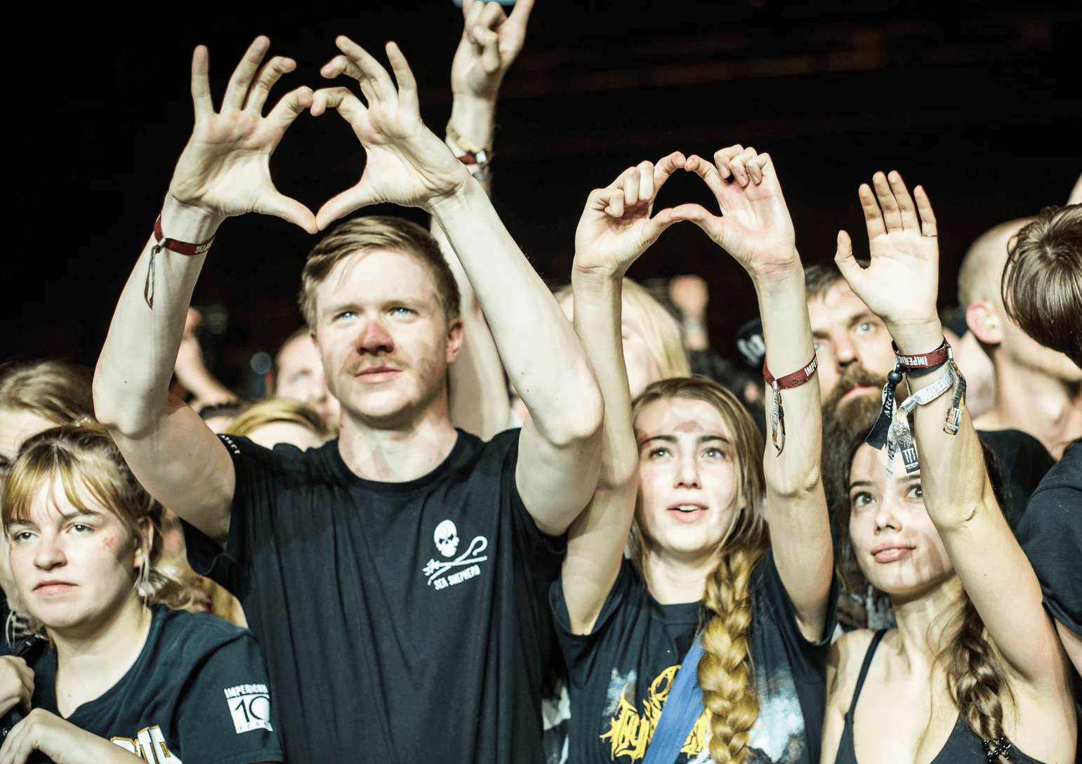 Three festival-goers forming a heart with their hands and raising it high into the air.