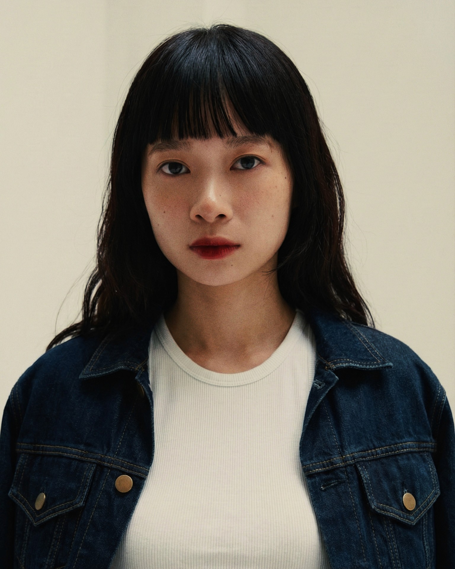 A thoughtful young person with dark hair gazes to the side, captured in soft black and white lighting.