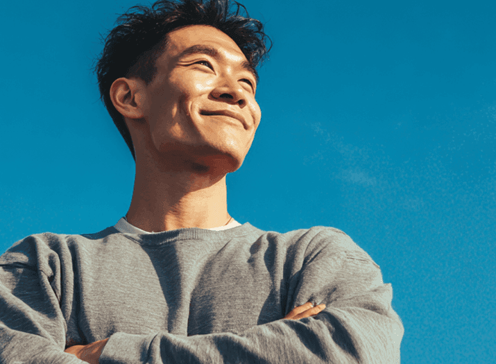 Homem sorrindo de braços cruzados com céu azul ao fundo.
