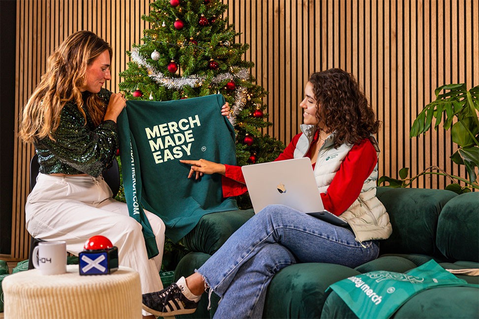 Monday Merch Office two employees looking at a monday merch sweater with the text merch made easy on it