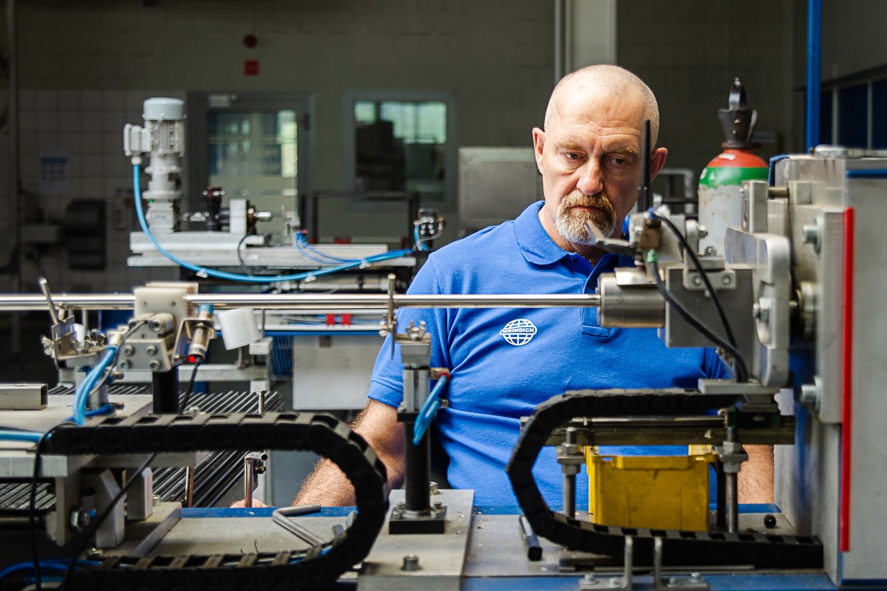 łysy z siwą brodą w niebieskiej polówce siedzi przy maszynie