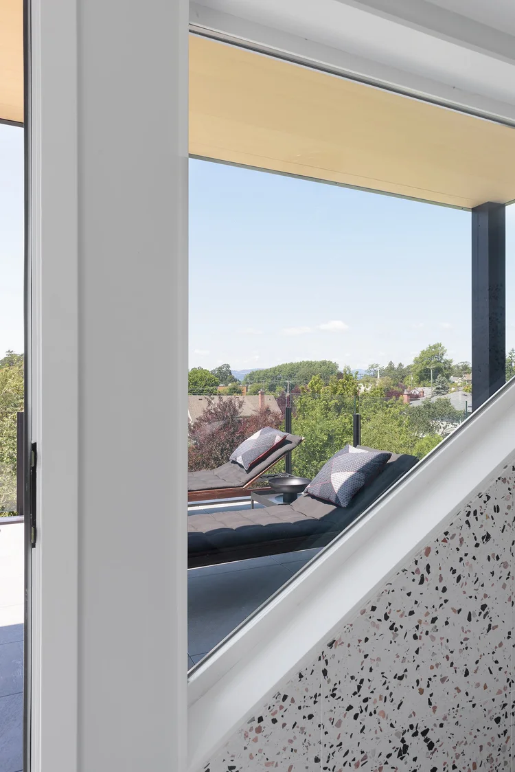 Modern two-story home with large glass windows, warmly lit interiors, and a balcony. Surrounded by trees and a manicured lawn at dusk. Cozy ambiance.