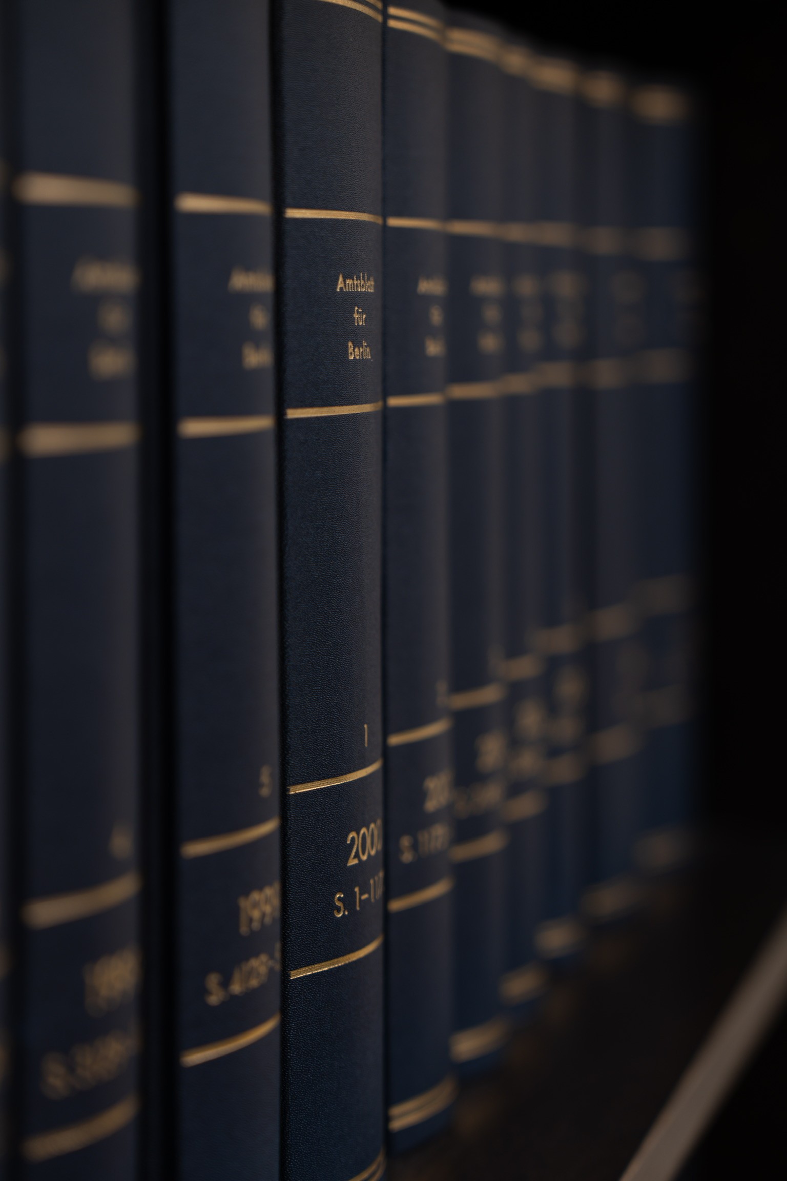 A smiling young man with crossed arms, wearing a plaid shirt and white t-shirt, poses against a dark background.