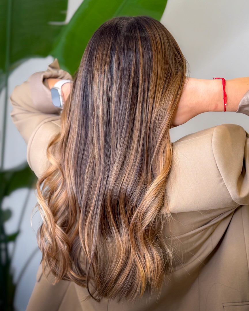 A woman with a white headband relaxing, her face illuminated by warm sunlight filtering through blinds, casting striped shadows. She has a serene and peaceful expression.