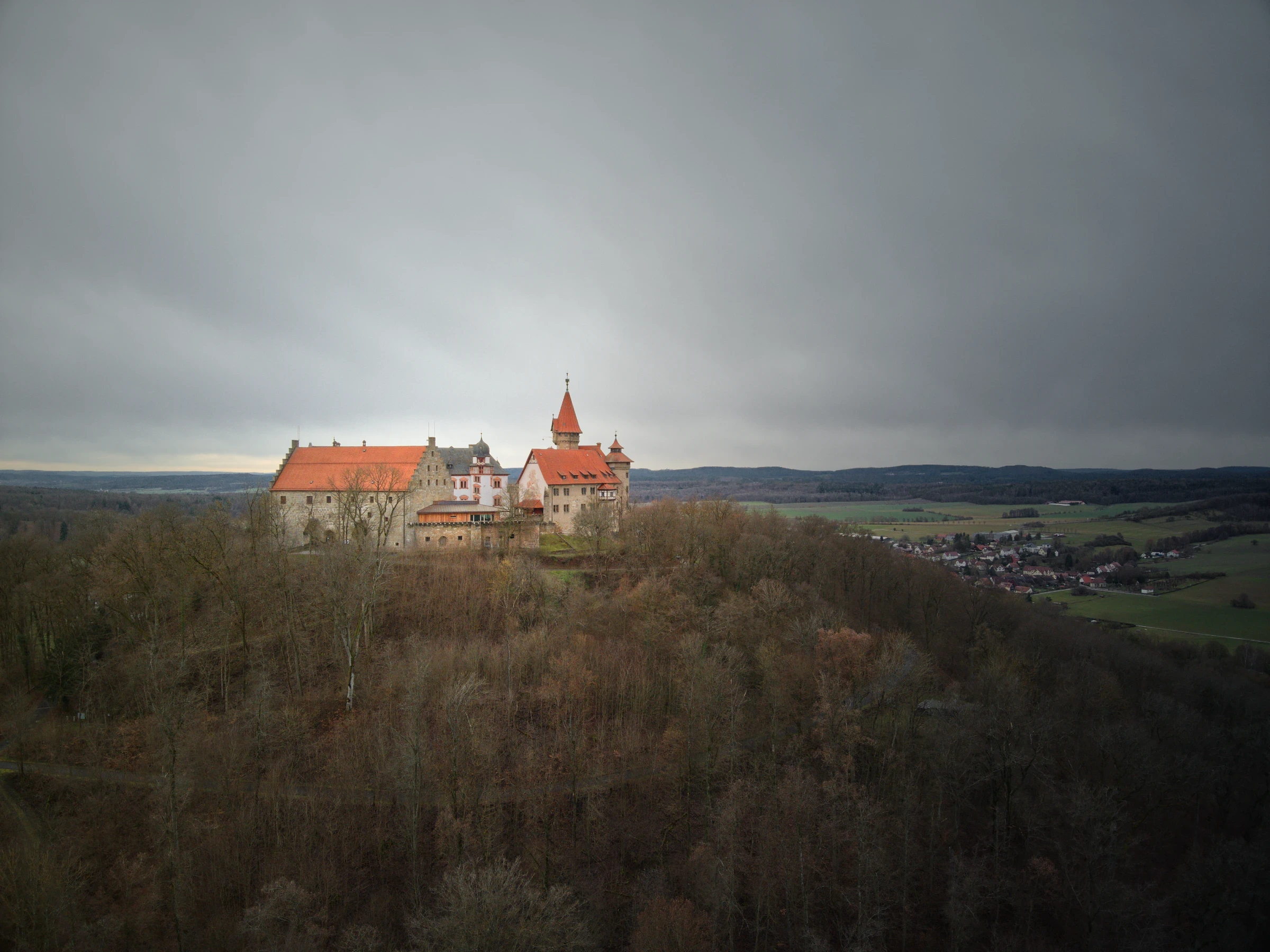 Drohnenaufnahme der Veste Heldburg eingebettet in die Hügellandschaft Südthüringens unter dramatischem Himmel.
