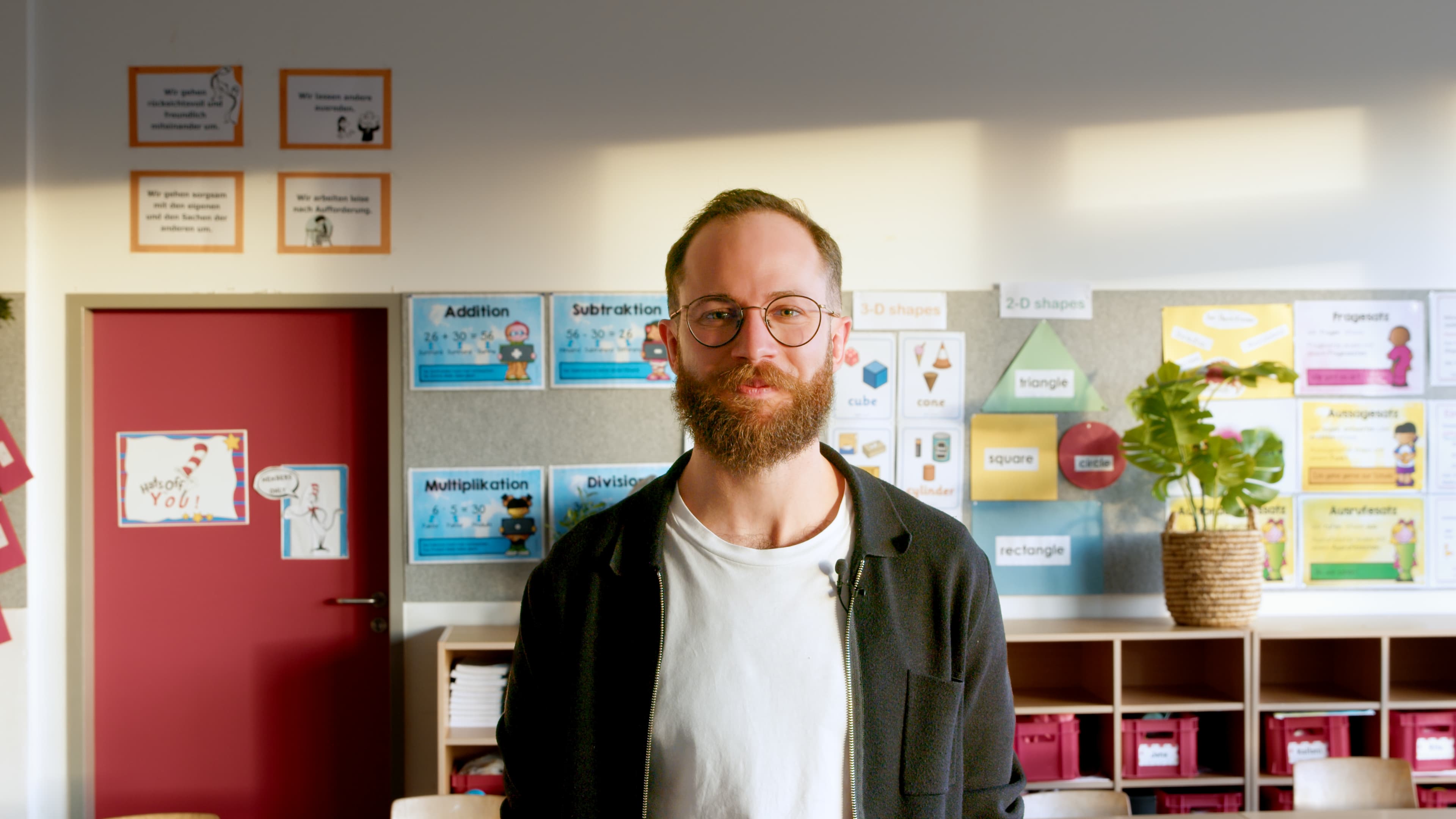 Male teacher in a colorful classroom with educational posters on the wall.