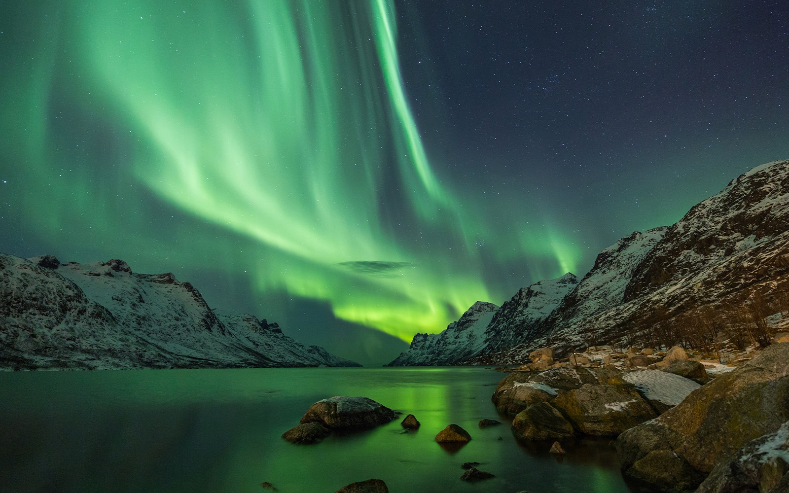 Northern lights over snowy mountains and a lake in Tromso.