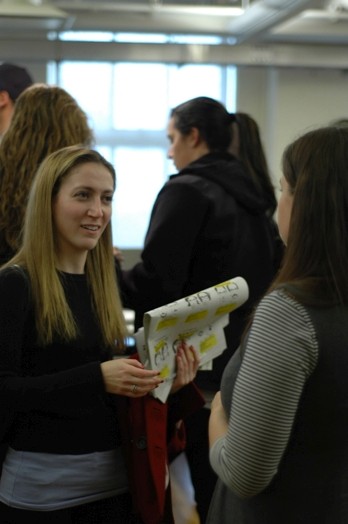 A photo of two girls talking while one of them is holding a folded poster.
