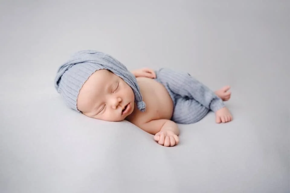 Sleeping newborn in a blue cap on a pale blanket