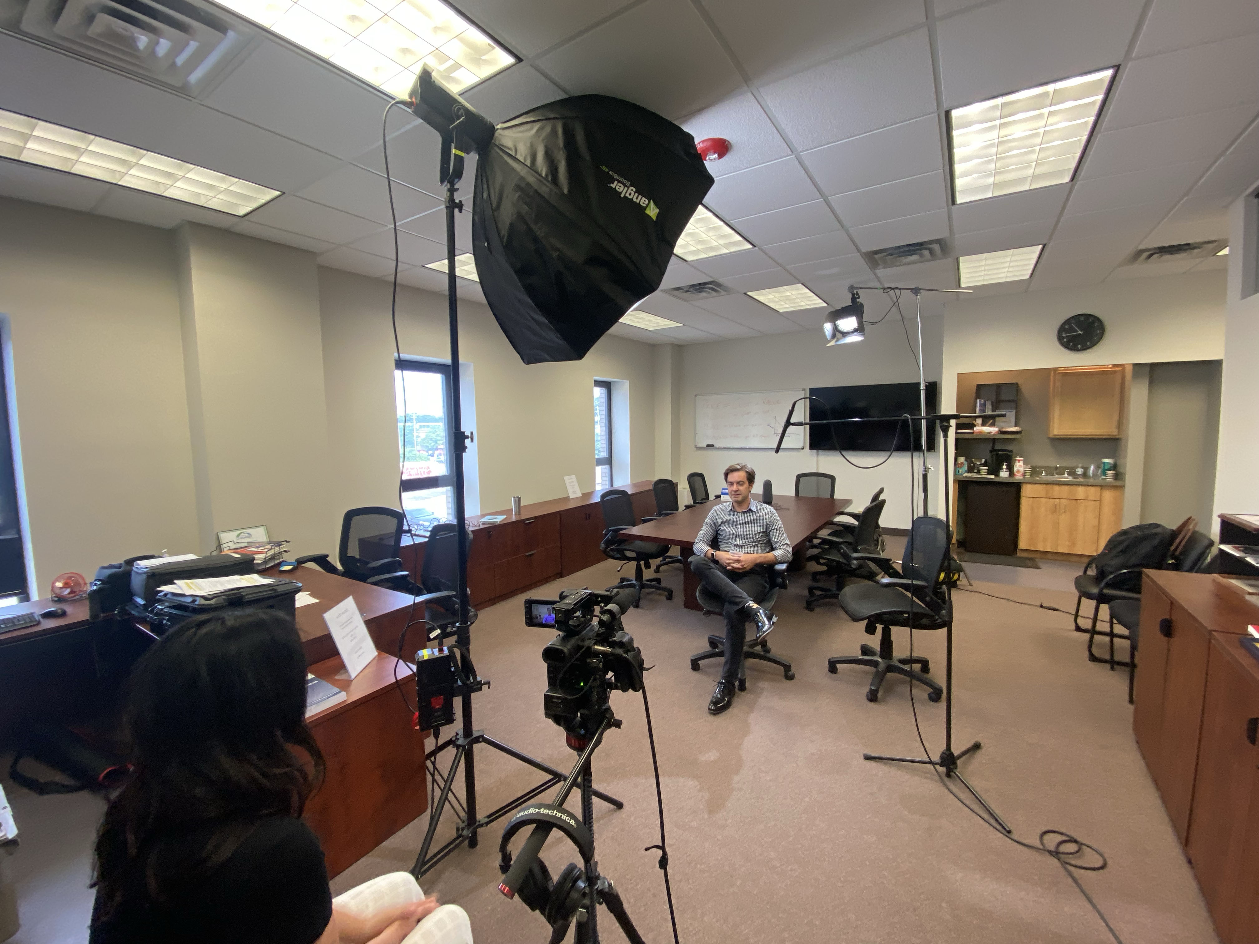 Video interview setup in a conference room with a camera on a tripod, studio lighting, and a subject seated.