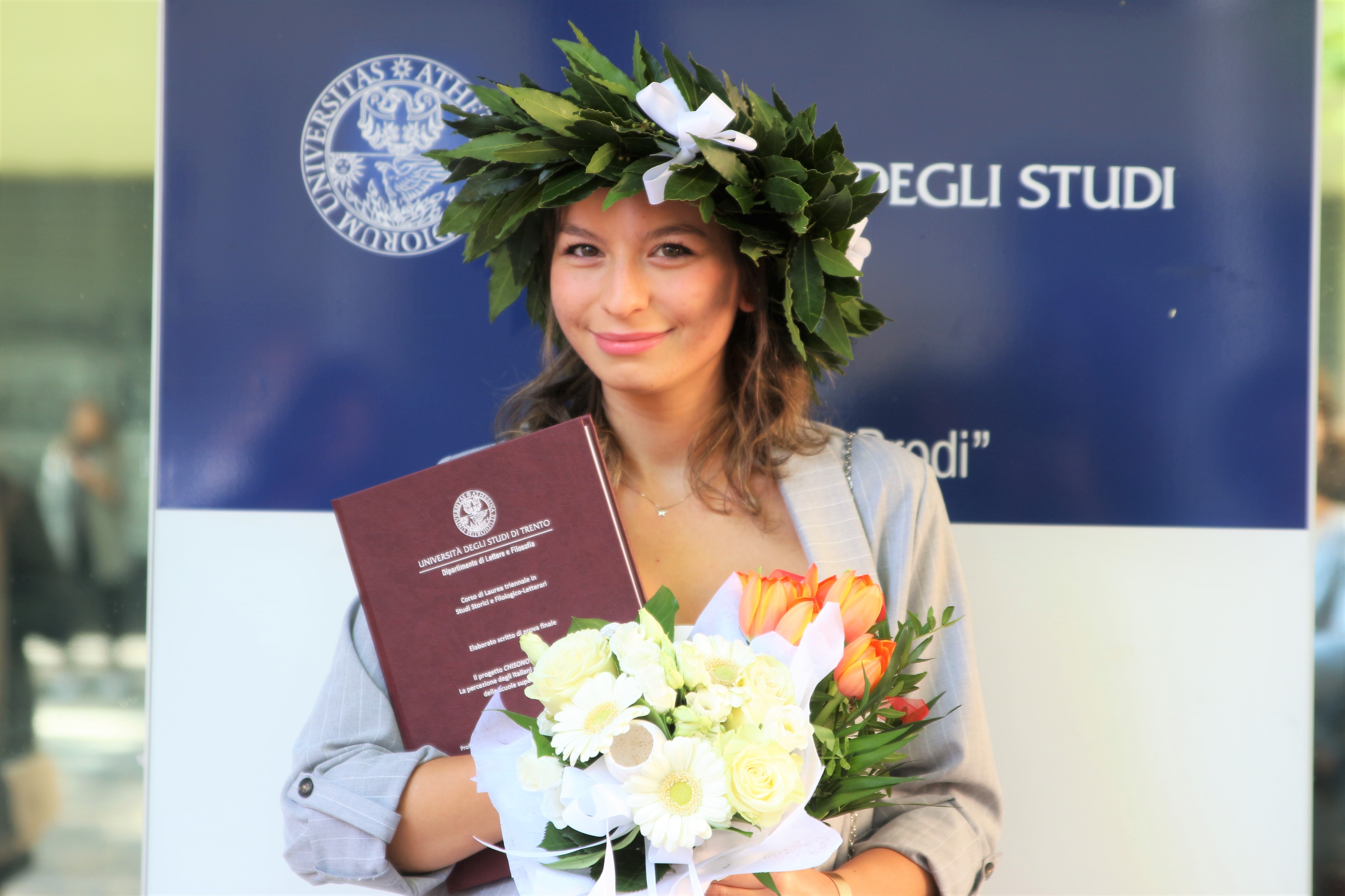 Silvia Vazzana con in testa una corona d'alloro e in mano la tesi di laurea triennale e un bouquet di fiori