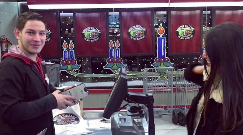 A photo of a man holding a phone near a cash register while a woman looks at it.