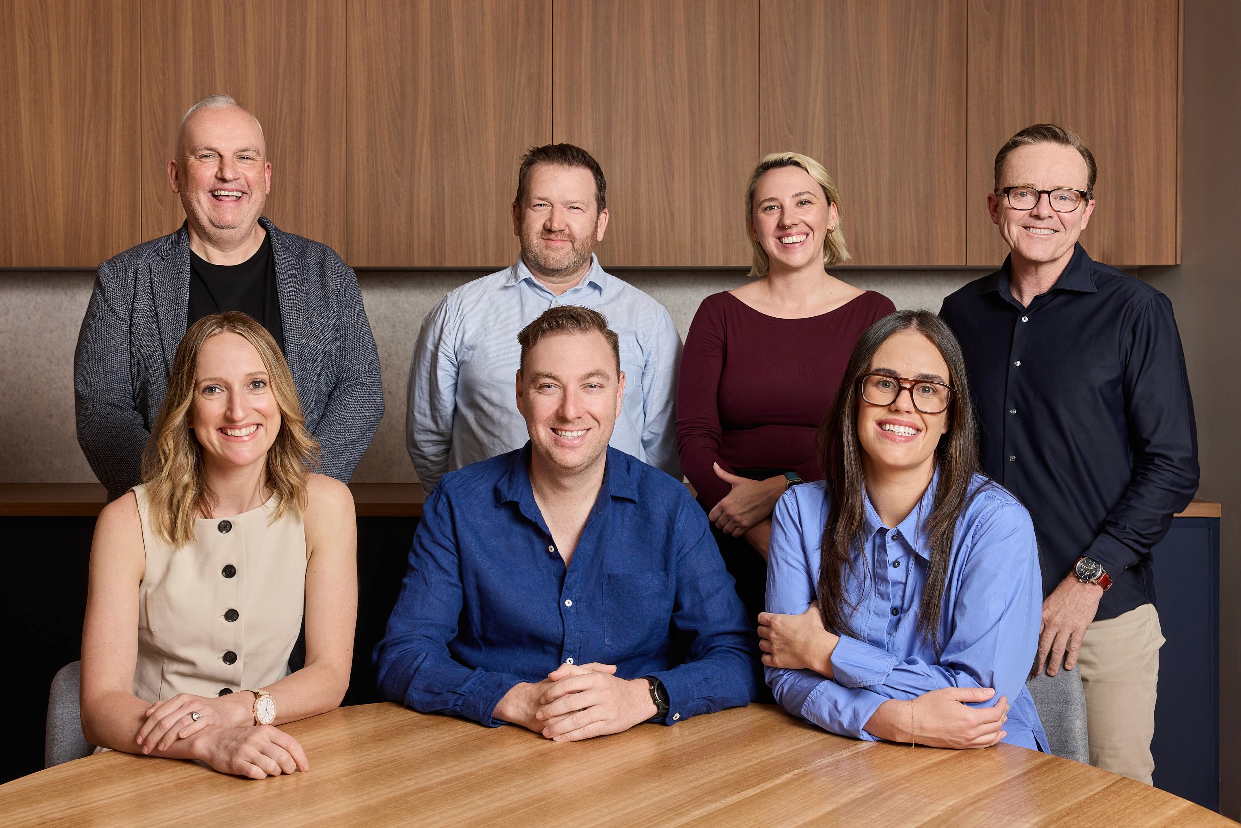 Silhouetted figures walking through a modern building hallway with glass windows and blinds reflecting light.