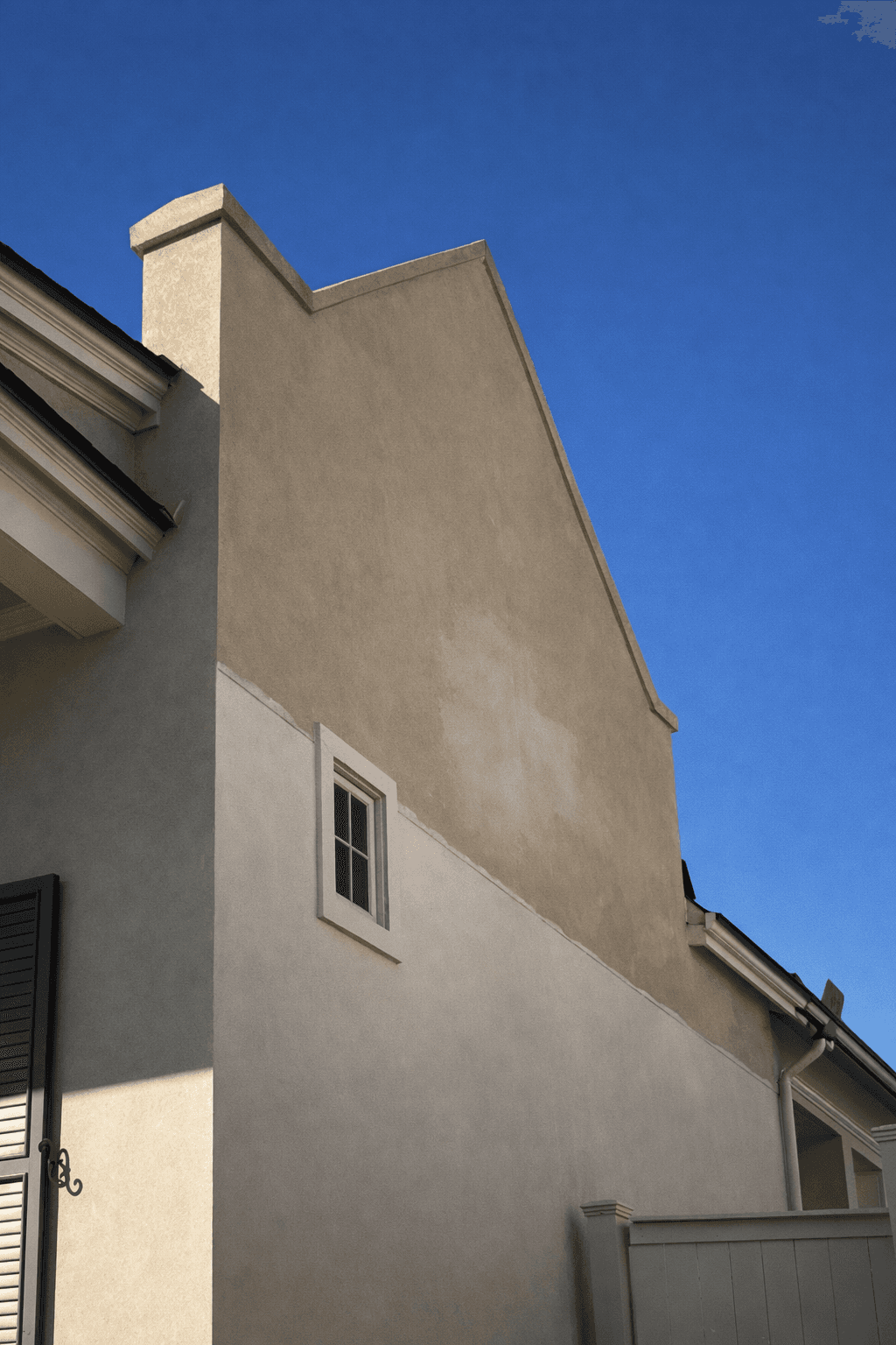 A modern, luxury beachfront villa with large glass windows and balconies overlooks a rocky shoreline, surrounded by palm trees at sunset.