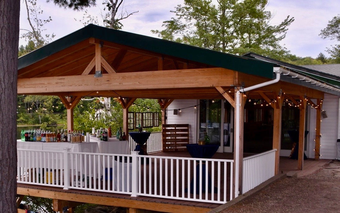 Covered lakeside porch pavilion with string lights and bar at Camp Lenox