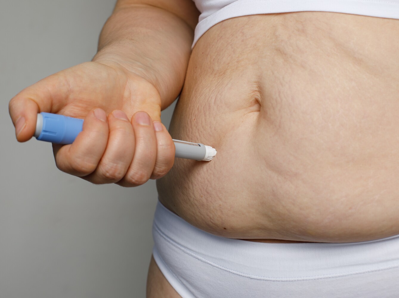 closeup of a woman injecting prescribed weight loss medicine into her stomach