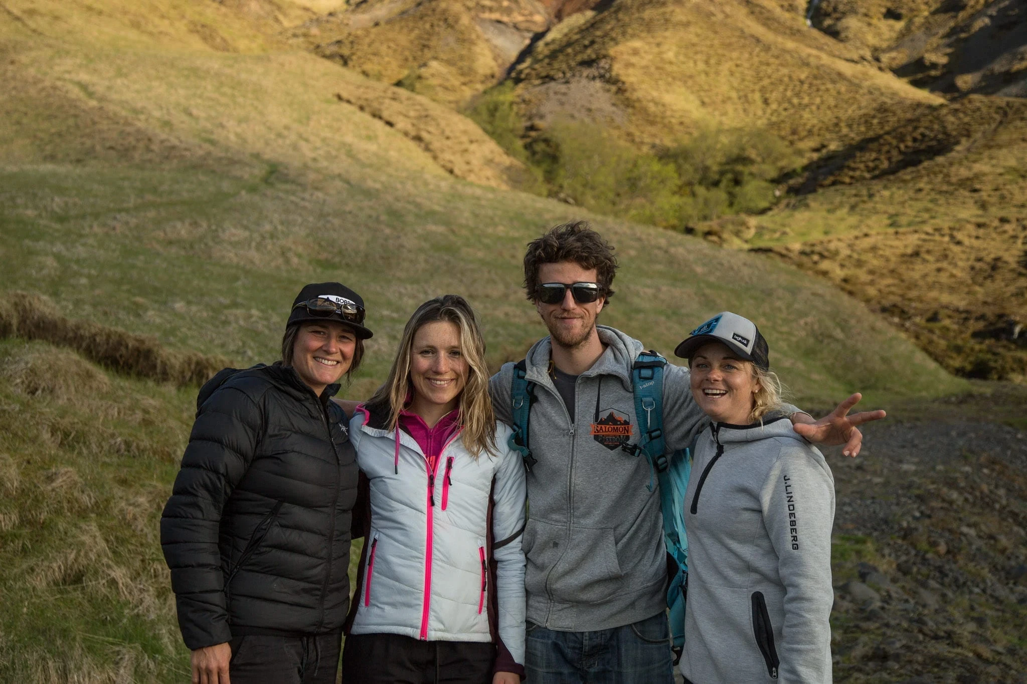 Four people smiling outdoors in a mountain valley, dressed in casual layers.