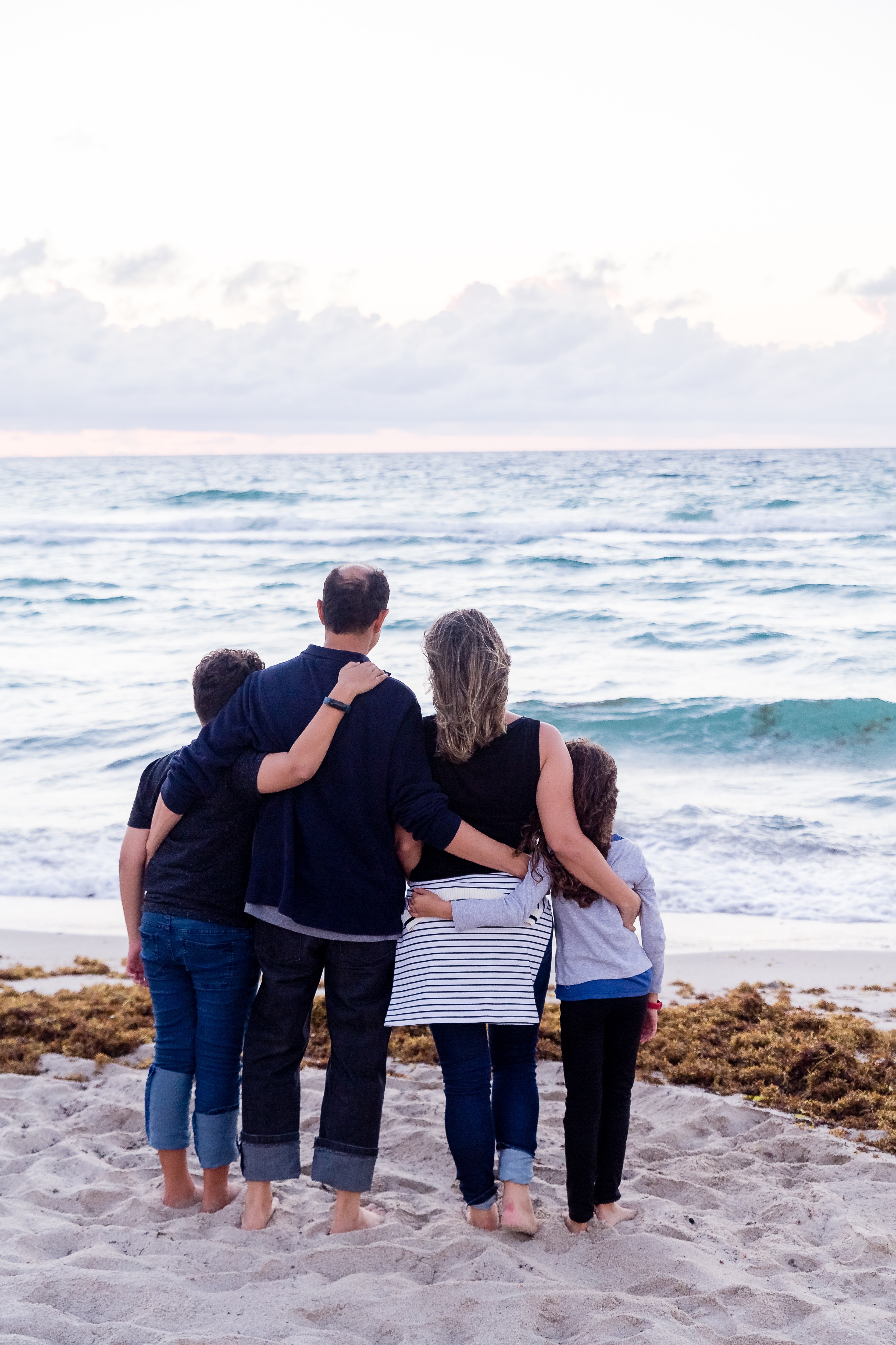 A family of four standing at beach looking out at sea - shoot from behind