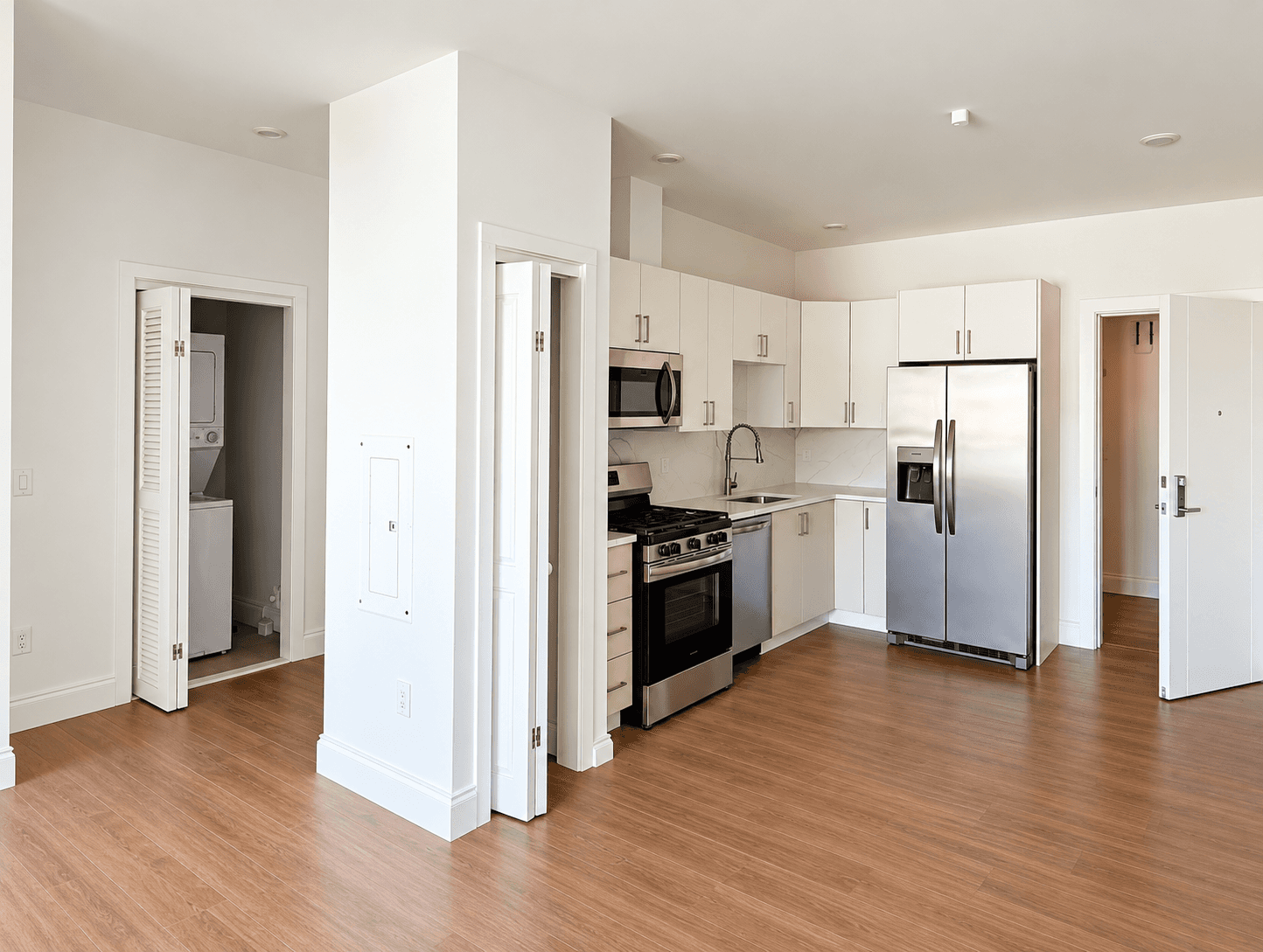 Finished kitchen with stainless steel appliances and an open in-unit washer-dryer closet on the left
