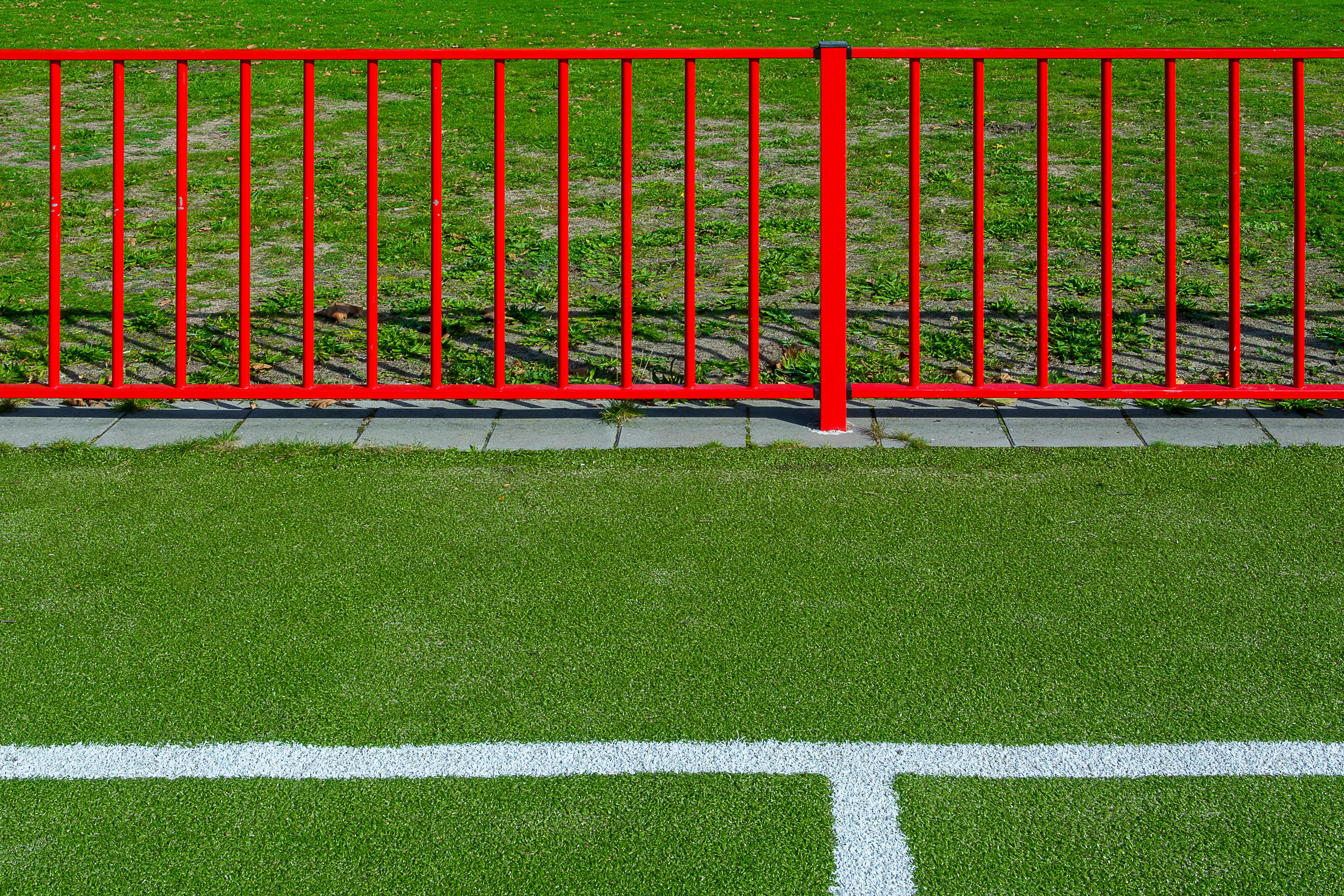 Red fence along green sports field boundary