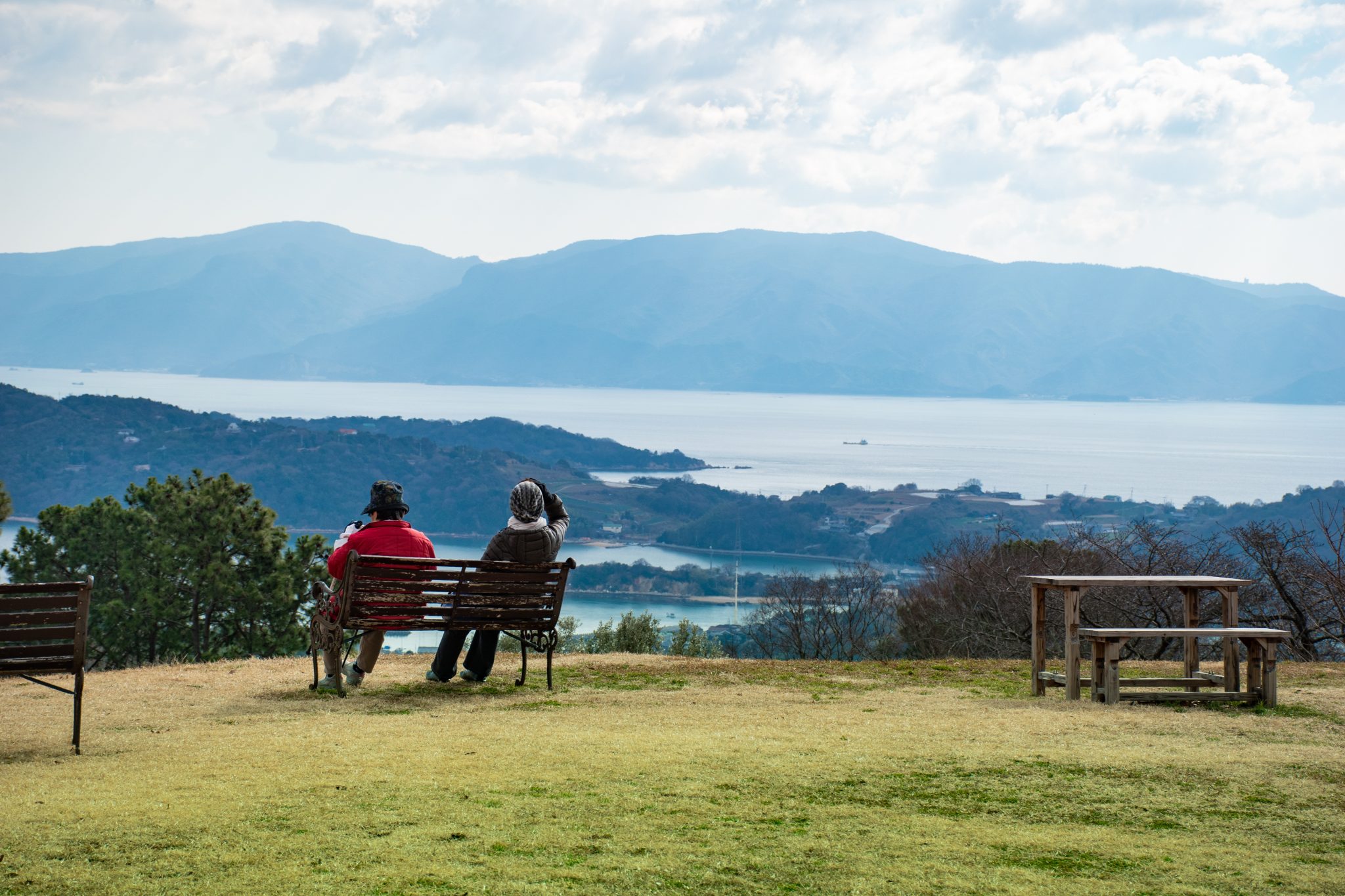 Two older women sitting on a bench in the olive grove, with a stunning view of the Seto sea