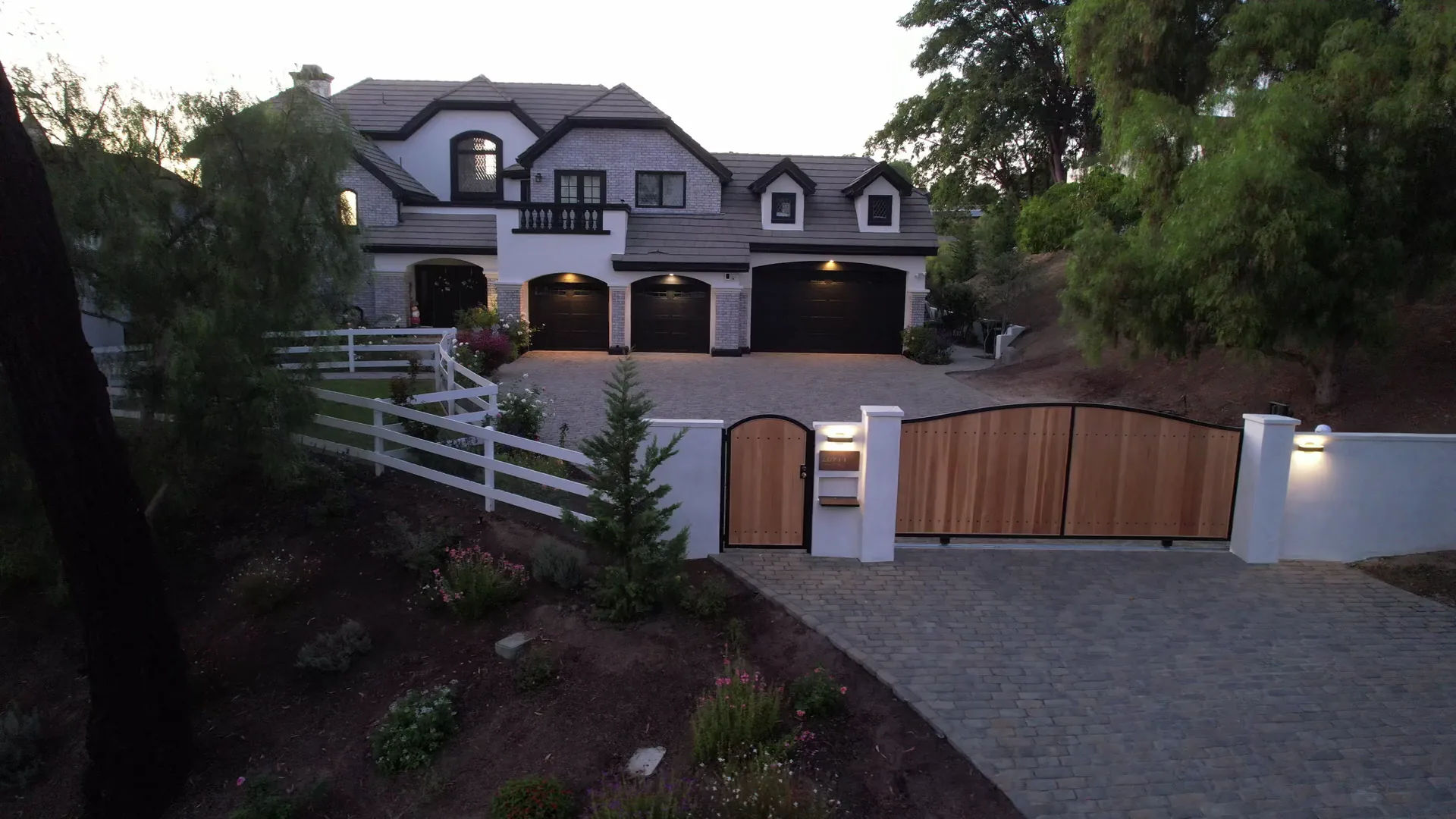 Paved driveway, entrance gates, boundary walls and planting in front of a two-story home.